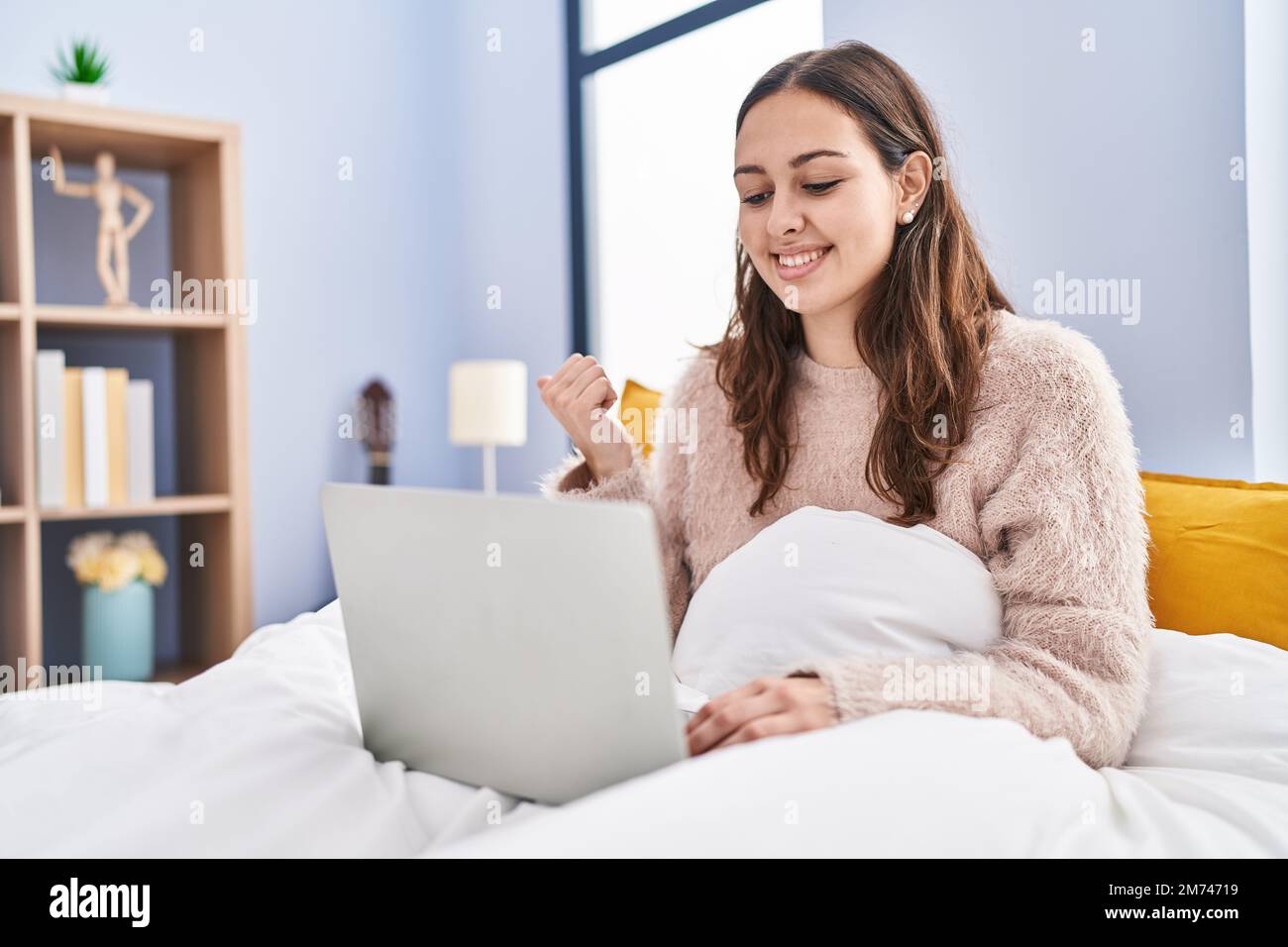 Young hispanic woman using computer laptop on the bed pointing thumb up ...