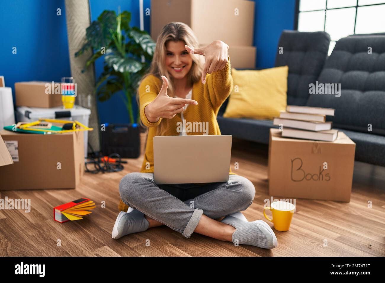Young woman sitting on the floor at new home using laptop smiling ...