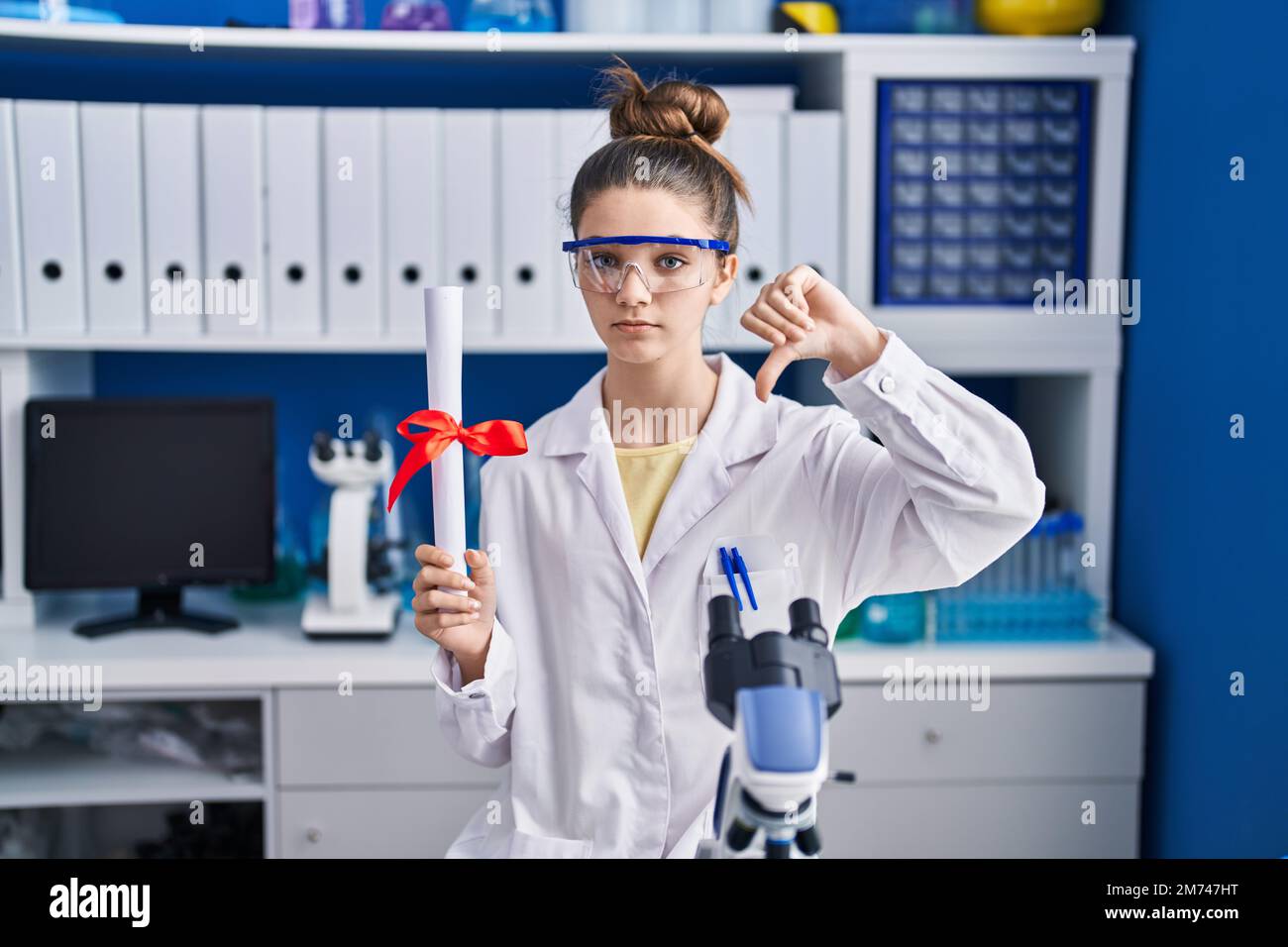 Teenager girl working at scientist laboratory holding degree with angry ...