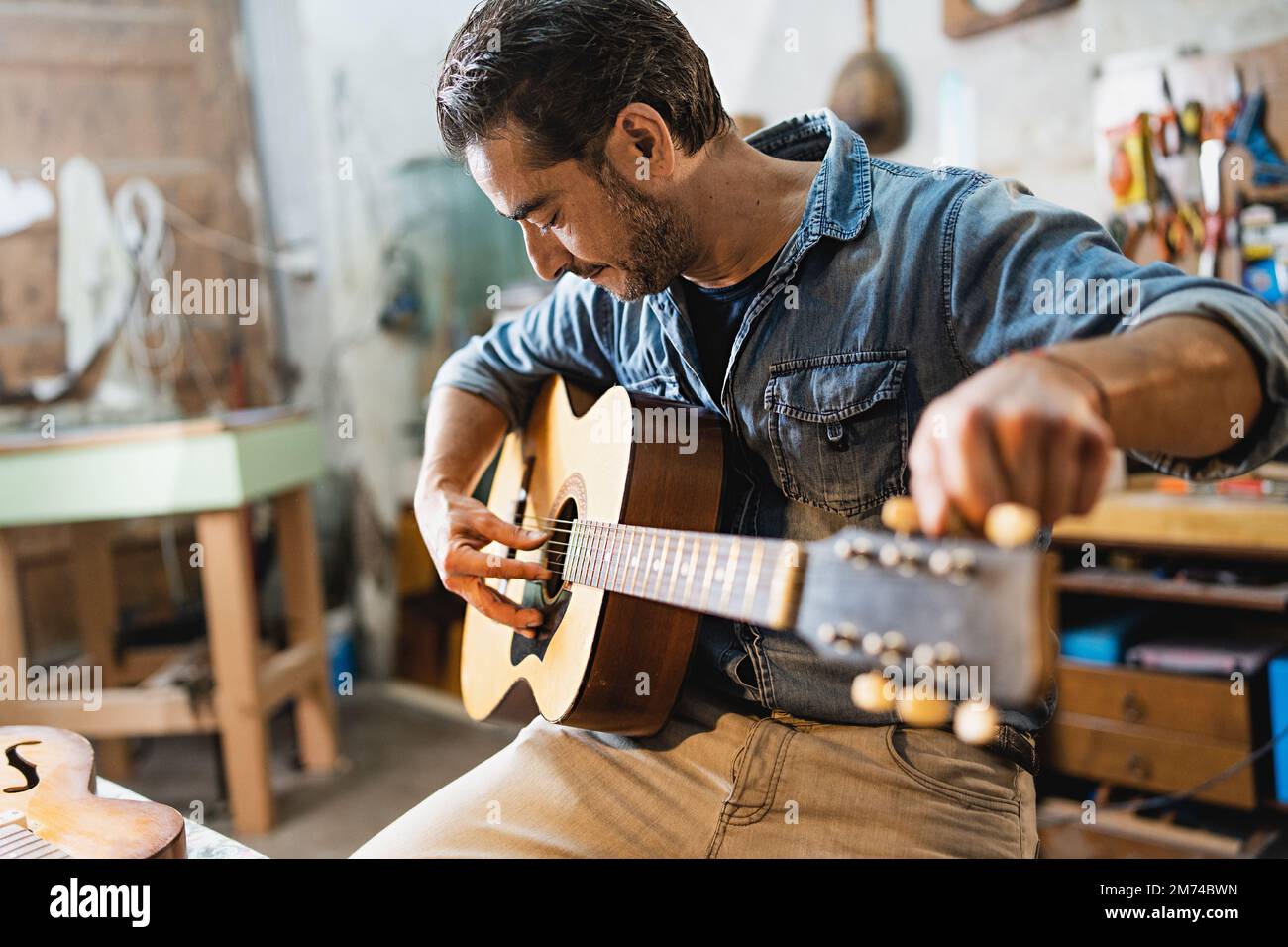 Adult man craftsman relaxing sitting on a chair and tuning an acoustic ...