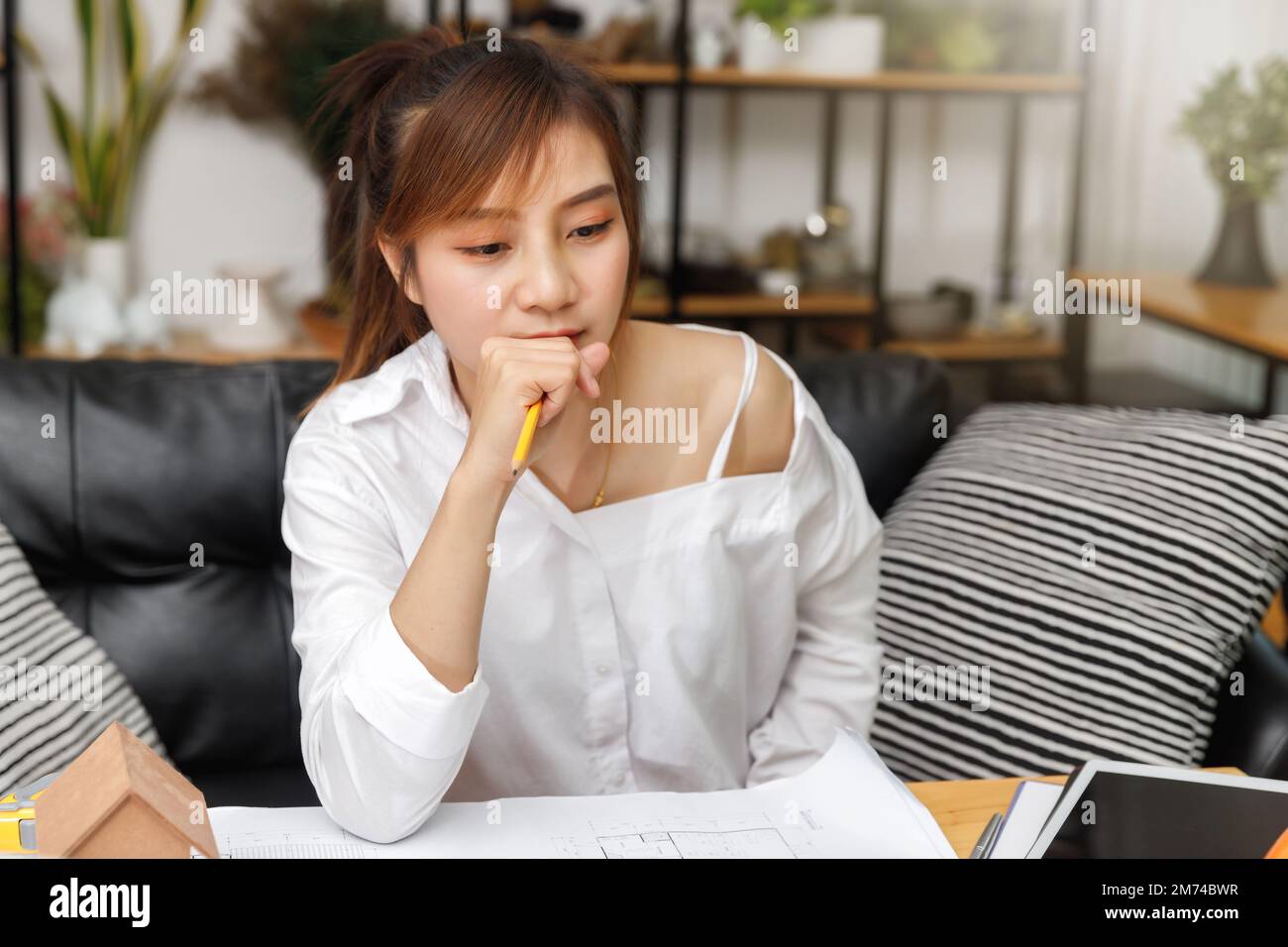 Thoughtful architect female holding a pencil and thinking over blueprint. Stock Photo