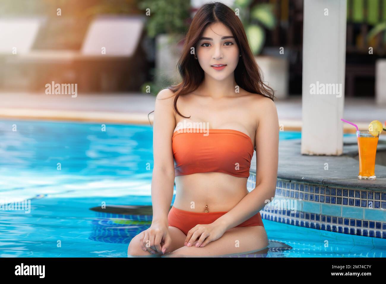 Sexy young asian woman in swimsuits in summer. beautiful woman in orange  bikini with tropical drink sitting in swimming pool Stock Photo