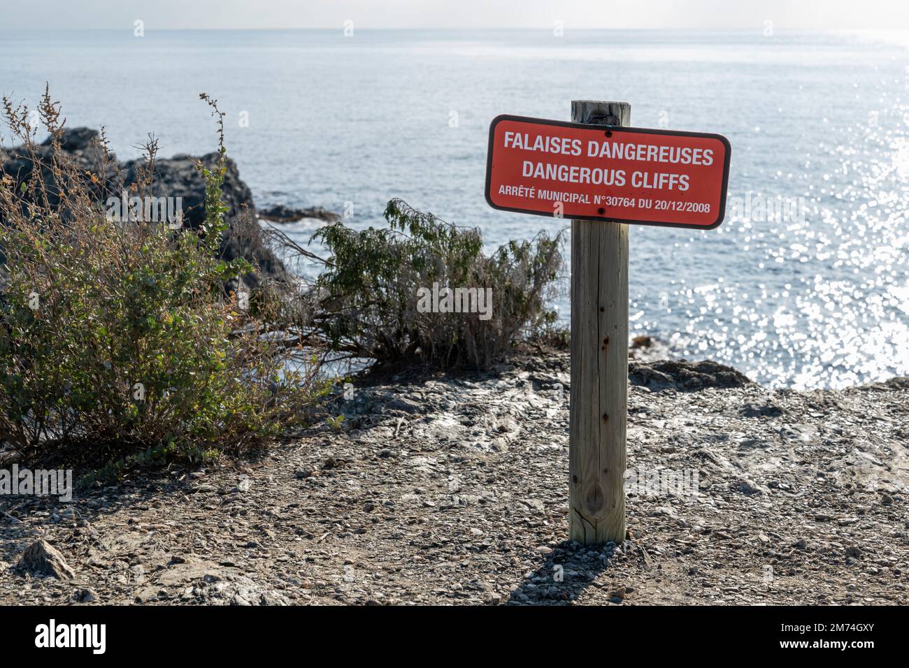 Red warning and information sign in South of France in front of cliffs and bilingual letters french english indicating Dangerous cliffs Stock Photo