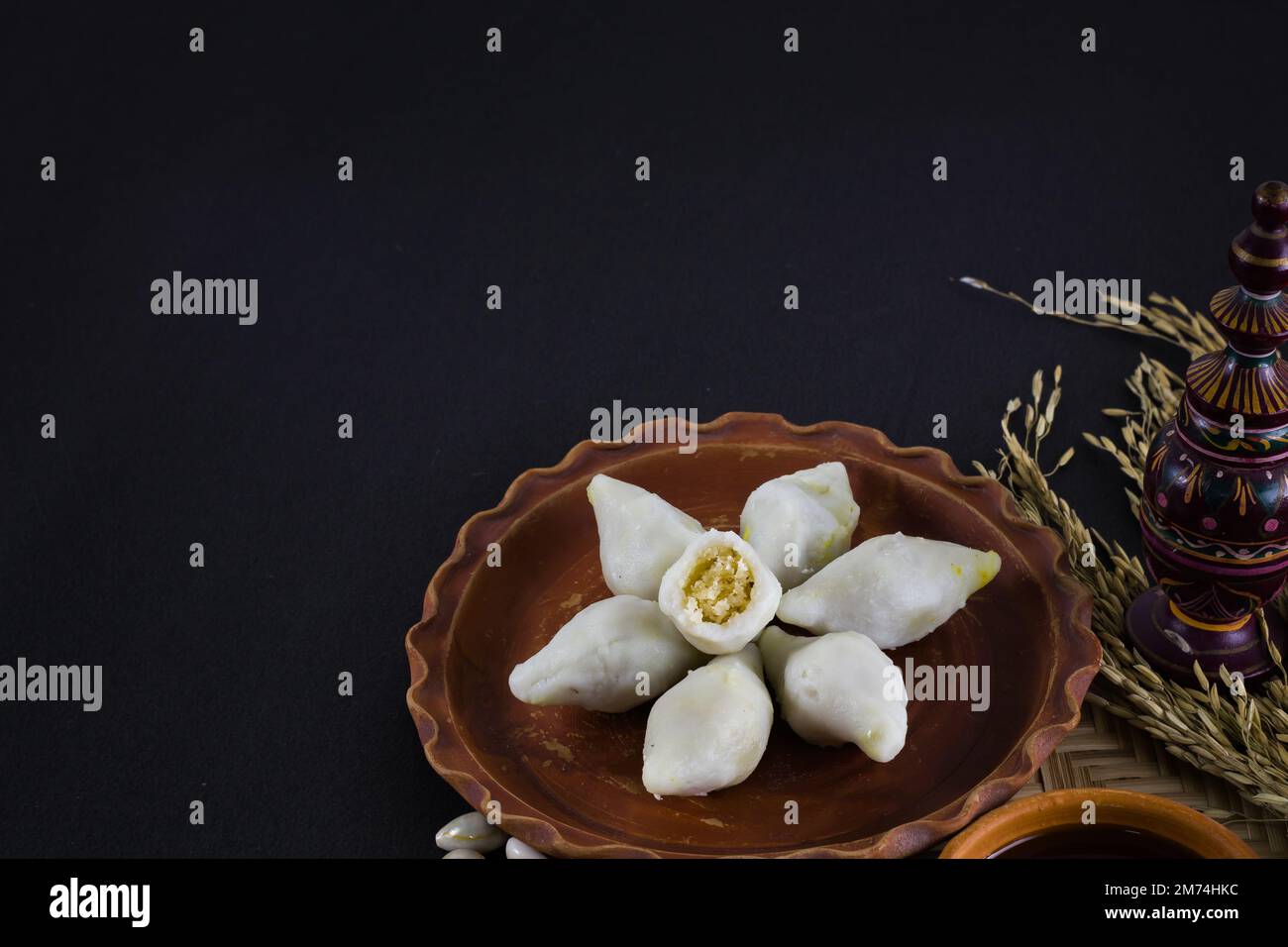 puli pithe or bengali rice flour dumplings with coconut fillings served on a clay plate with jaggery. shot against black background.this traditional d Stock Photo