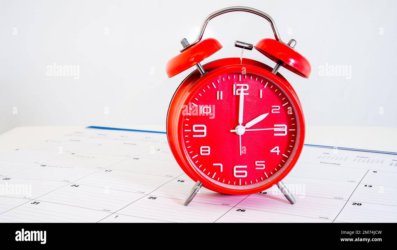 Red clock standing on calendar with white background behind Stock Photo