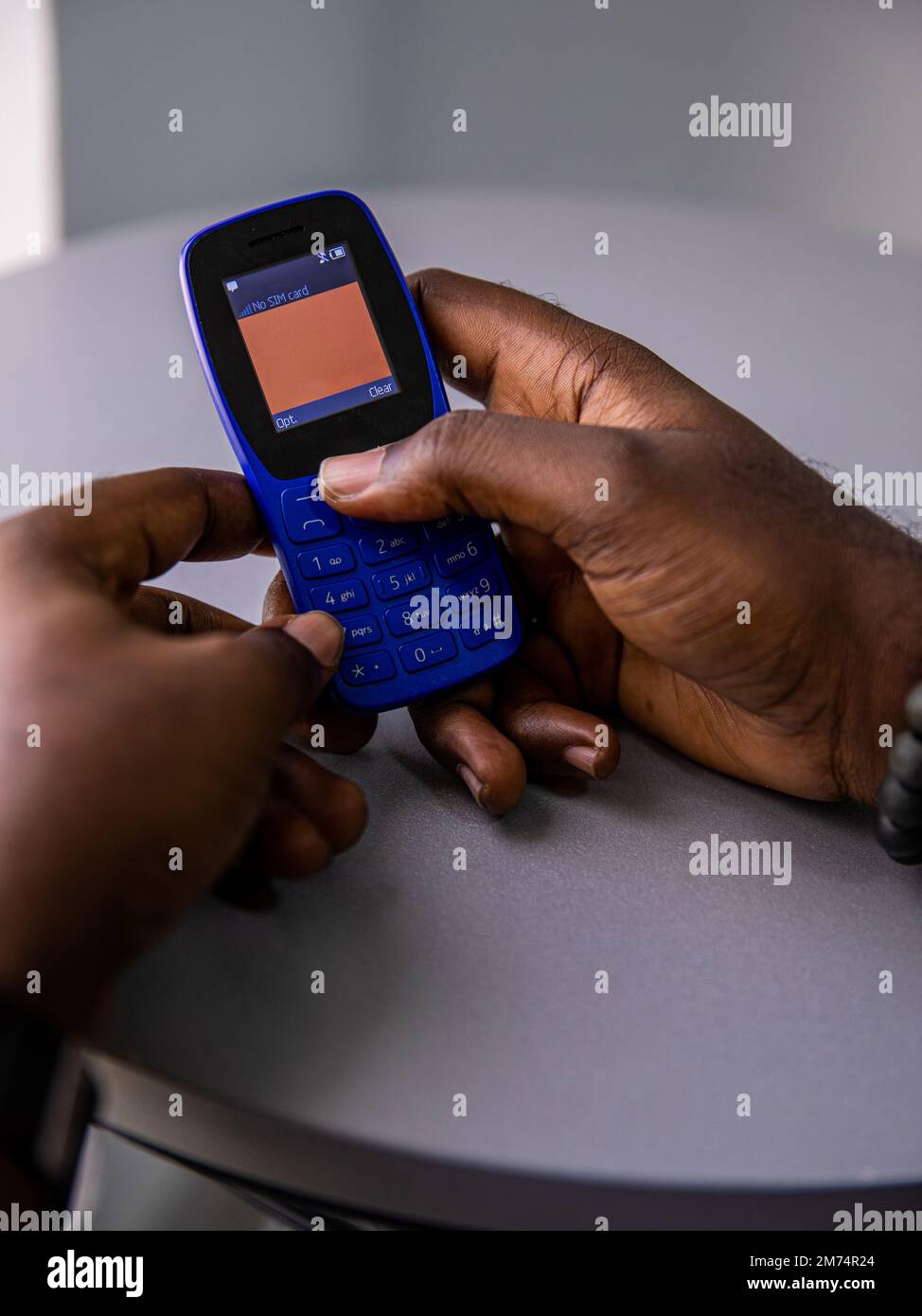 A vertical shot of a dark-skinned person holding a blue feature phone ...