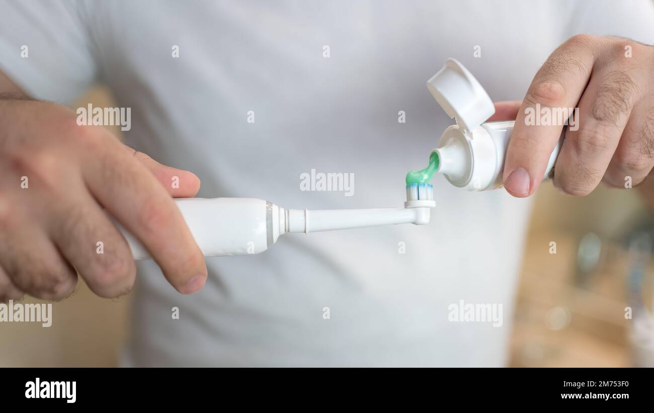 White man's hands pouring thootpaste into an electric toothbrush. Stock Photo