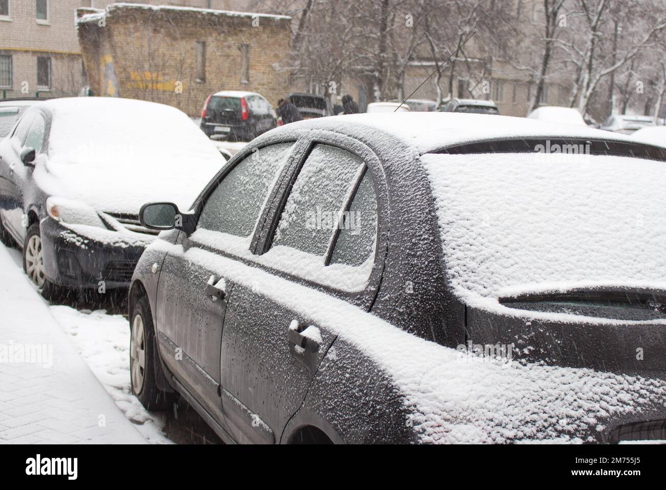 Cars in snow at the streets. First snow in the city. Traffic in winter. Bad weather and transport. Snow covered car. Snowfall in town. Car parking in Stock Photo