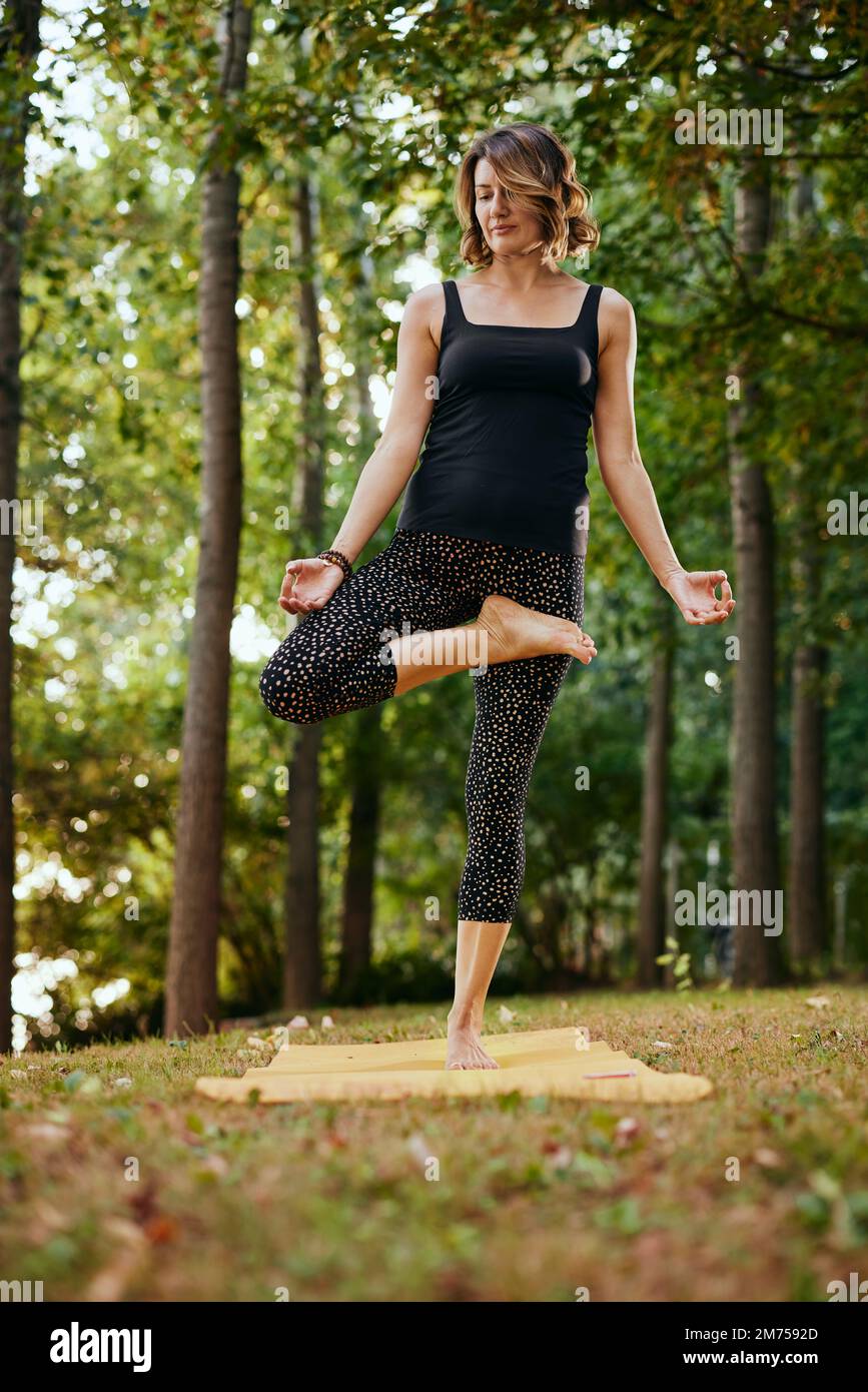 A slim woman practices yoga in the forest in autumn. She is in the