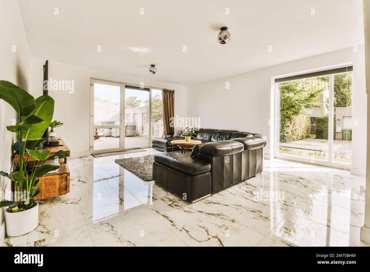 a living room with white marble flooring and black leather couches in