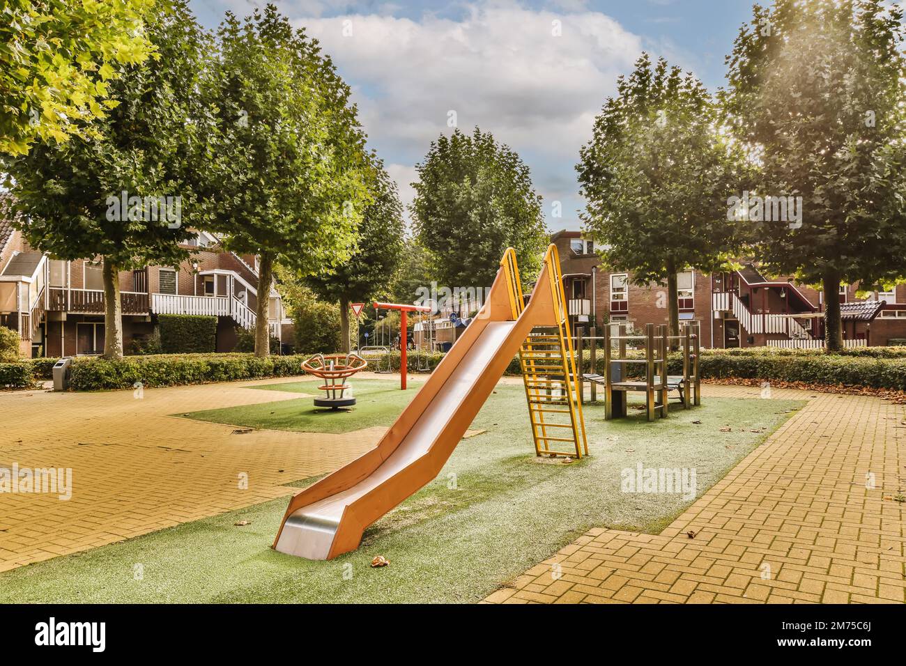 a playground with a slide in the middle school's play area, surrounded by trees and green lawns Stock Photo