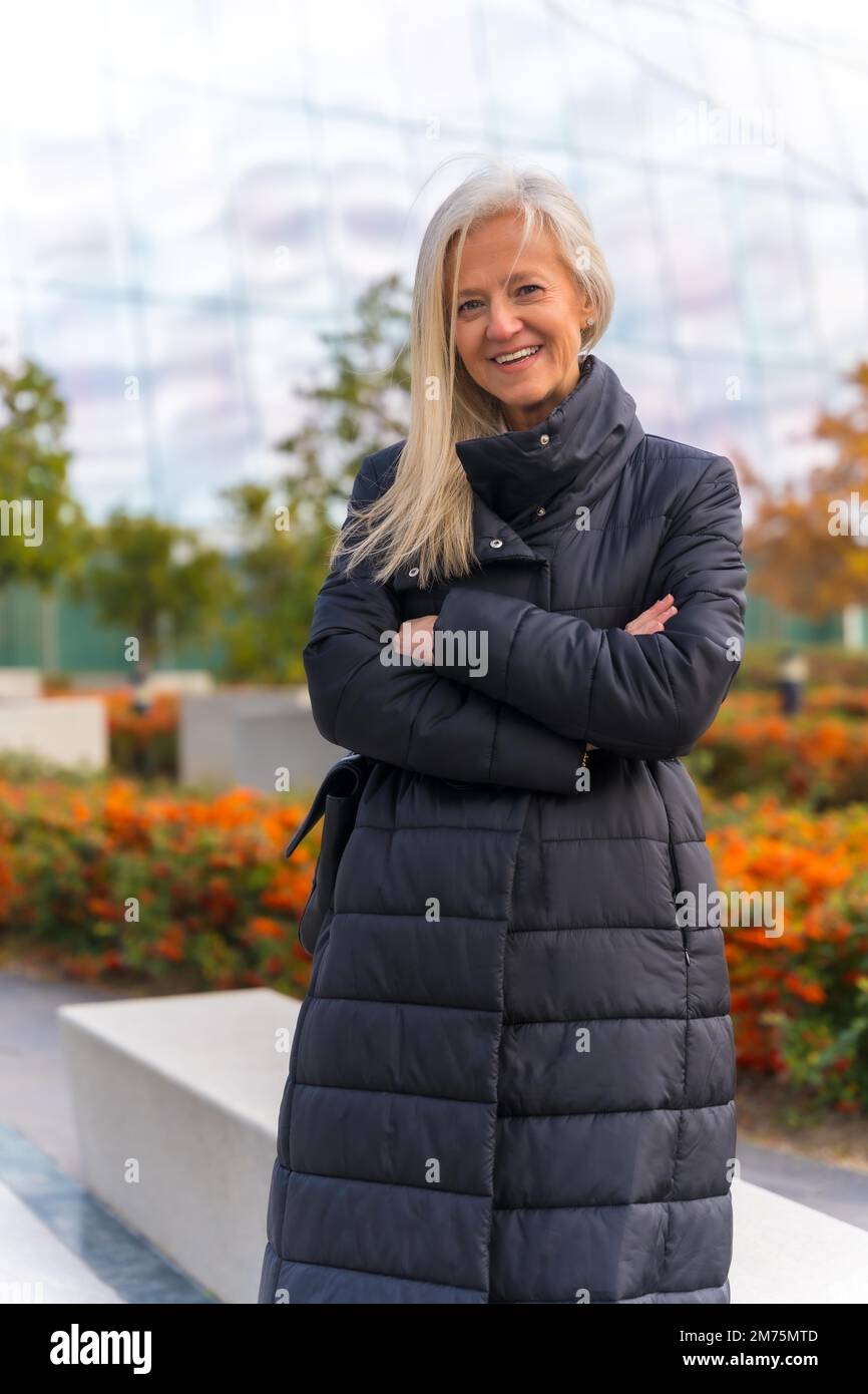 Corporate portrait of white-haired middle-aged businesswoman, standing by skyscraper office Stock Photo