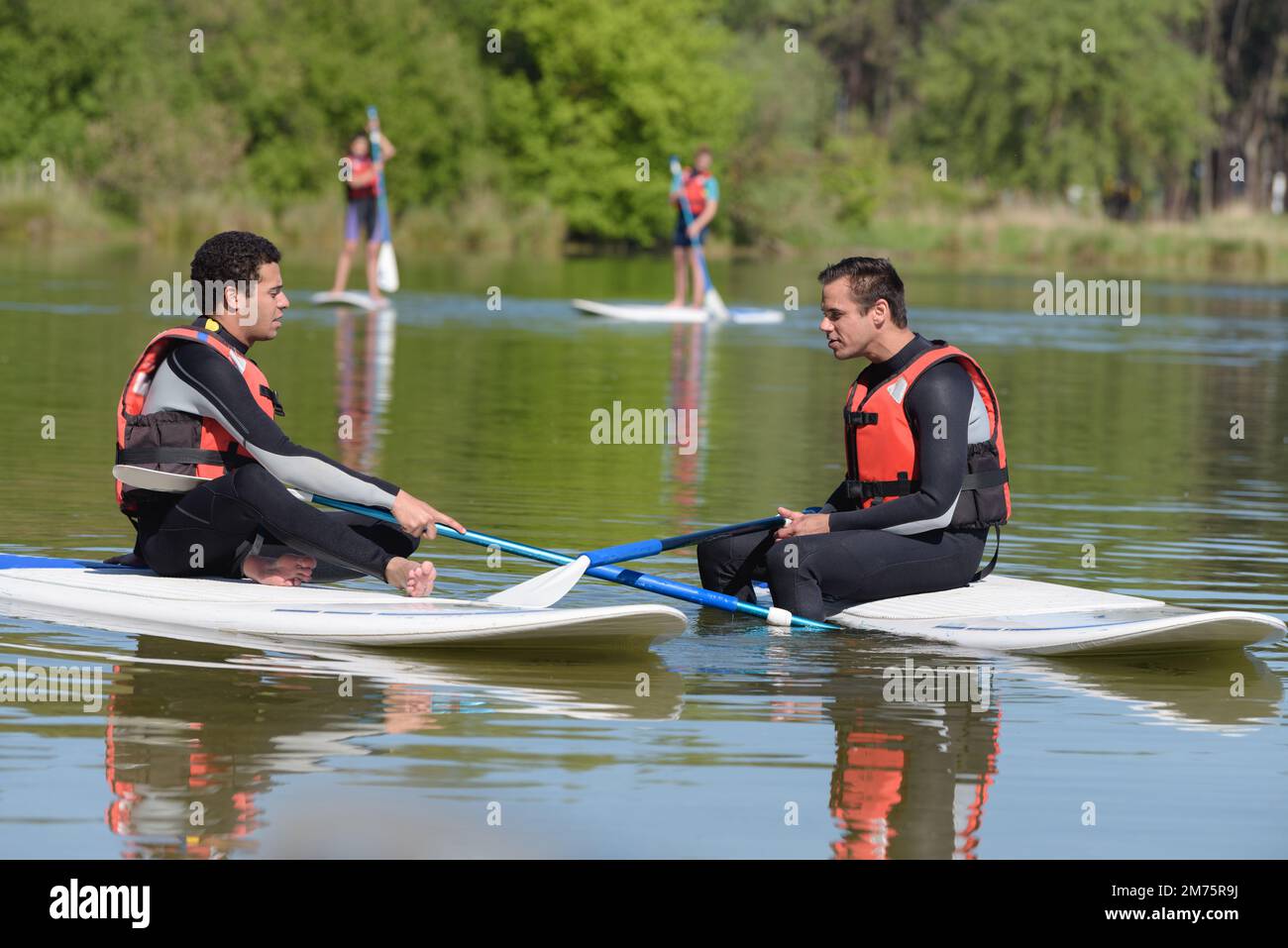 two men wearing wetsuits sat on paddle boards Stock Photo Alamy