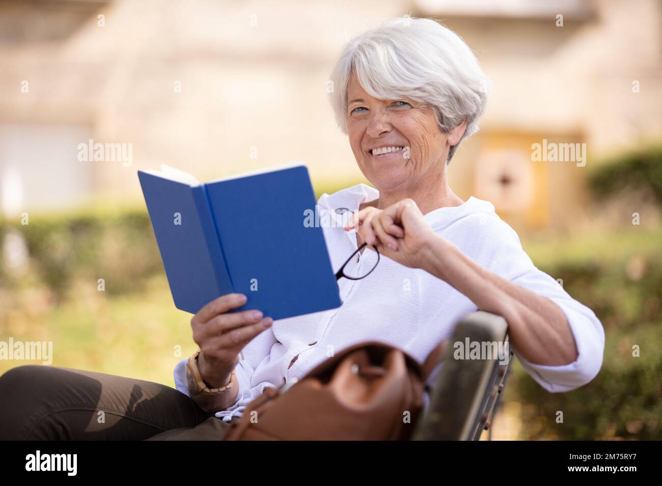 senior woman sat on park bench reading a book Stock Photo - Alamy