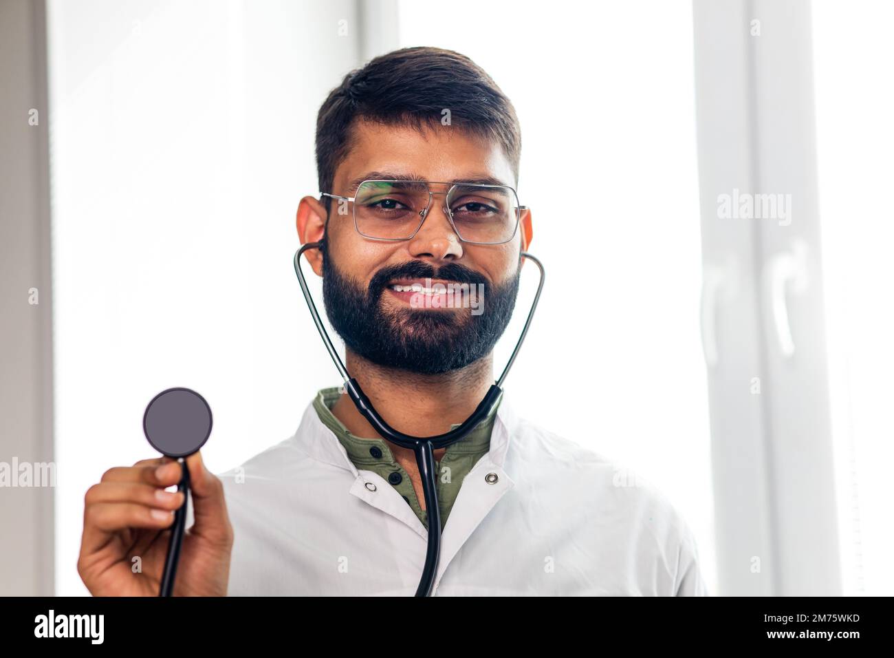 Portrait of male indian doctor wearing white coat in clinic office Stock Photo