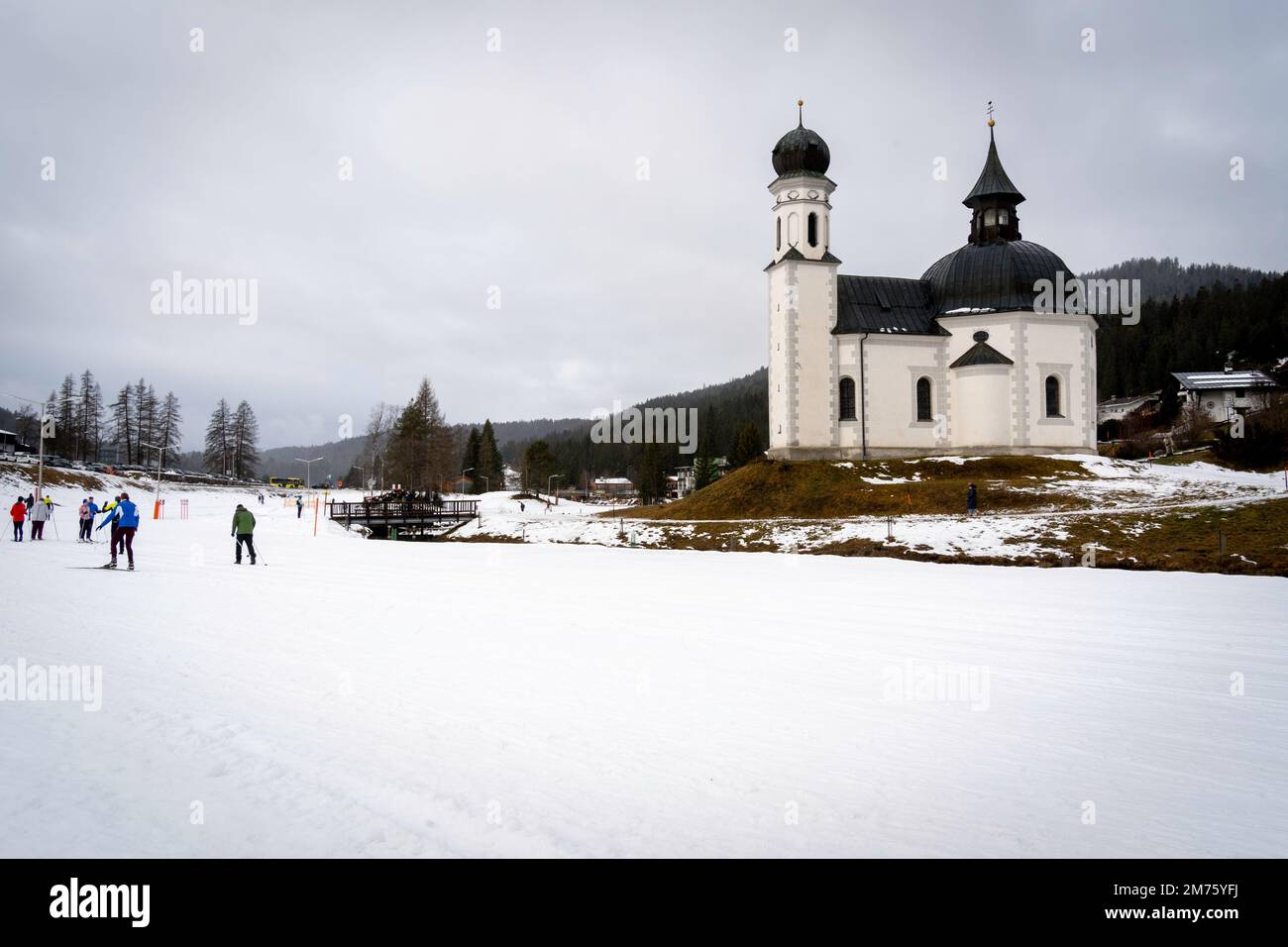 Seefeld, Austria - December 2022: Crosscrountry skiers (in motion blur) skiing near the Seekirchl chapel (also known as Heiligkreuzkirche) in Seefeld Stock Photo