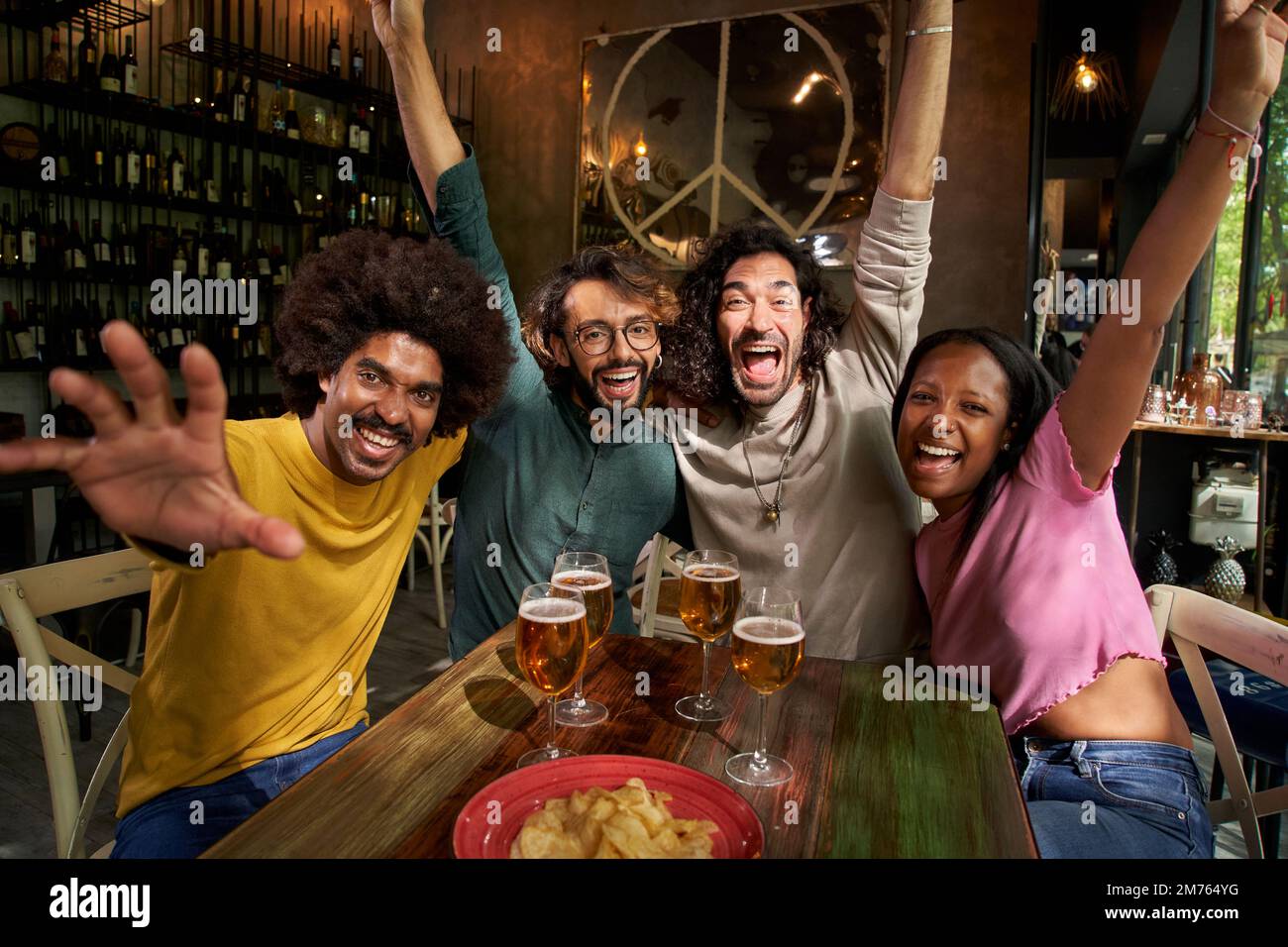 Group of four cheerful young friends taking selfie inside bar Happy