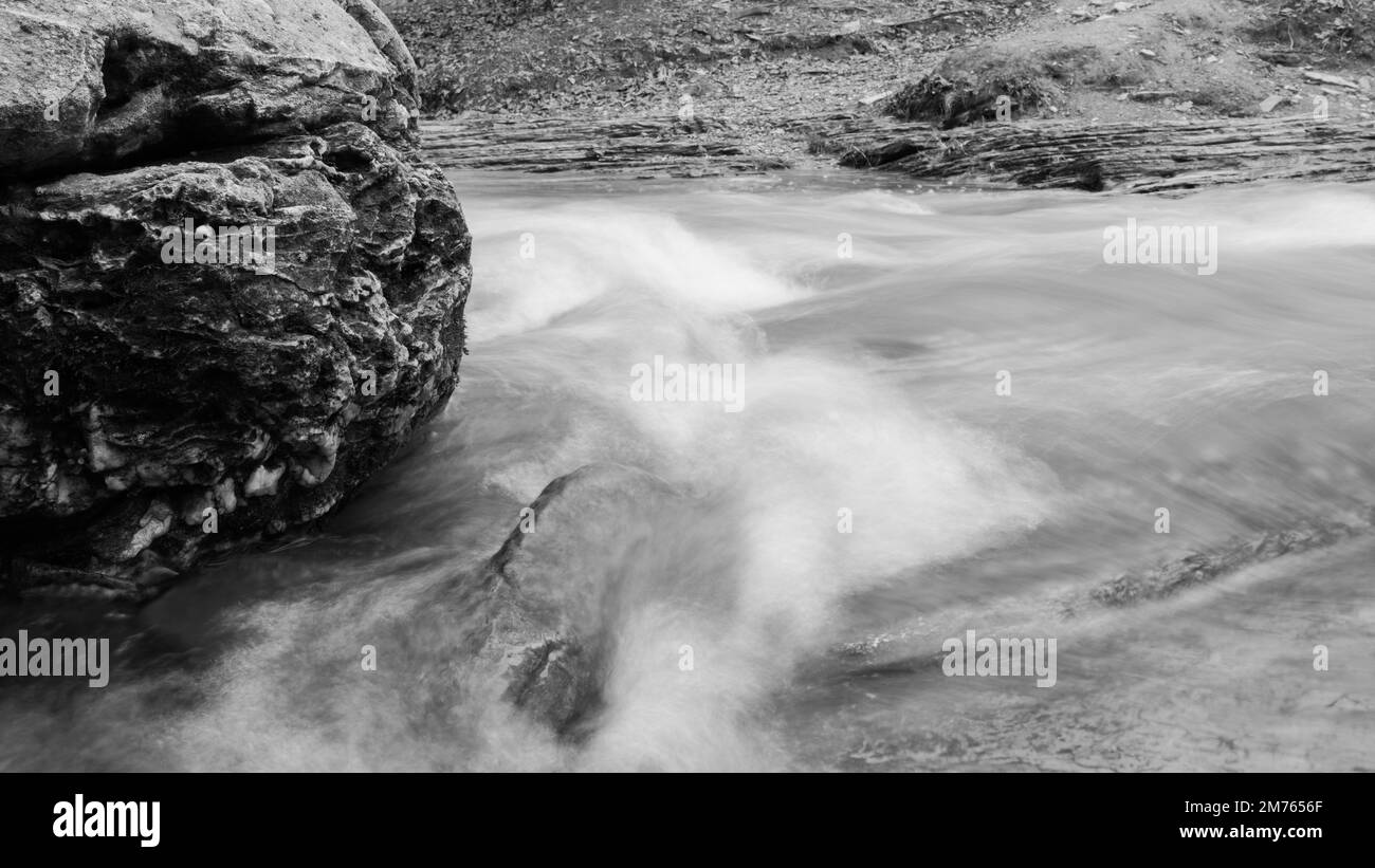 Black and white image of creek water rushing and swirling following a ...