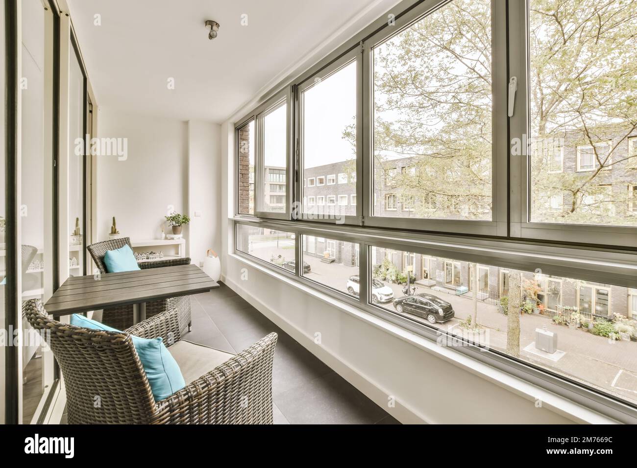 a balcony with wickers on the chairs and table in front of large windows looking out onto an urban street Stock Photo