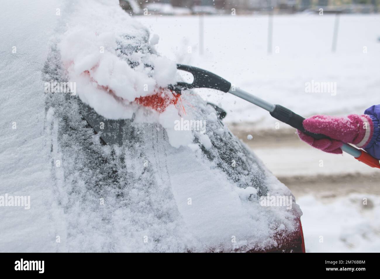 Process of cleaning a car from snow in the morning, girl removing snow from windscreen with a