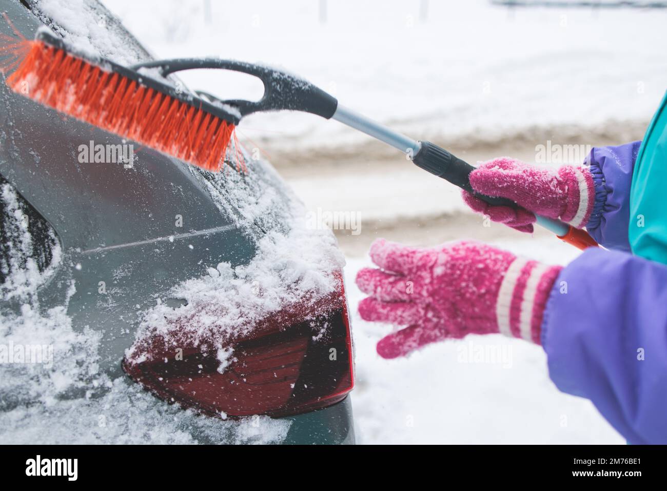 Process of cleaning a car from snow in the morning, girl removing snow from windscreen with a