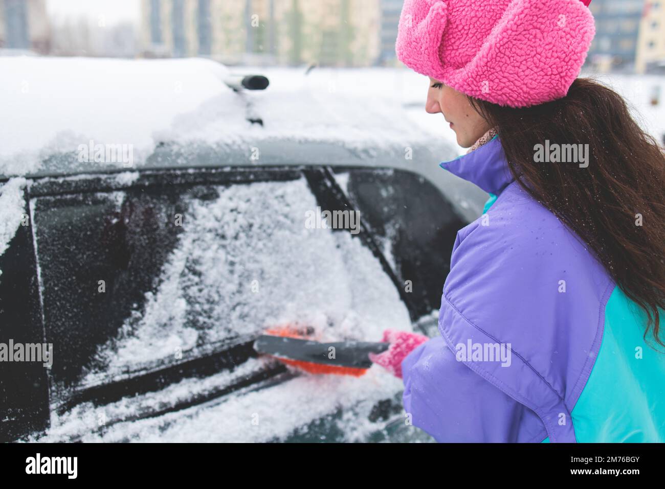 Process of cleaning a car from snow in the morning, girl removing snow from windscreen with a