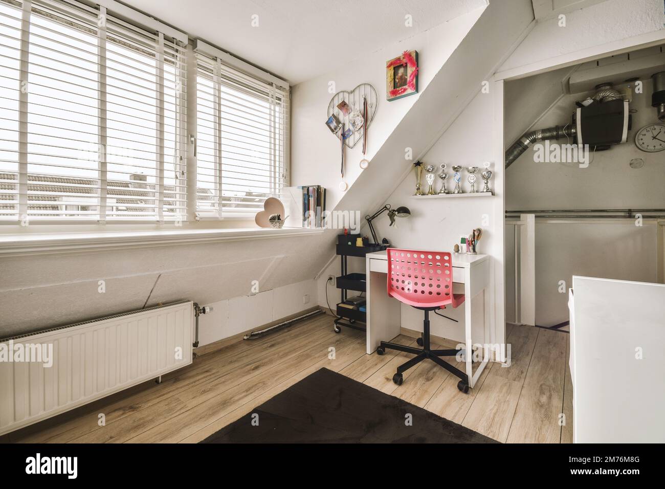 a room with wooden floors and white walls, there is a small desk in the corner next to the window Stock Photo