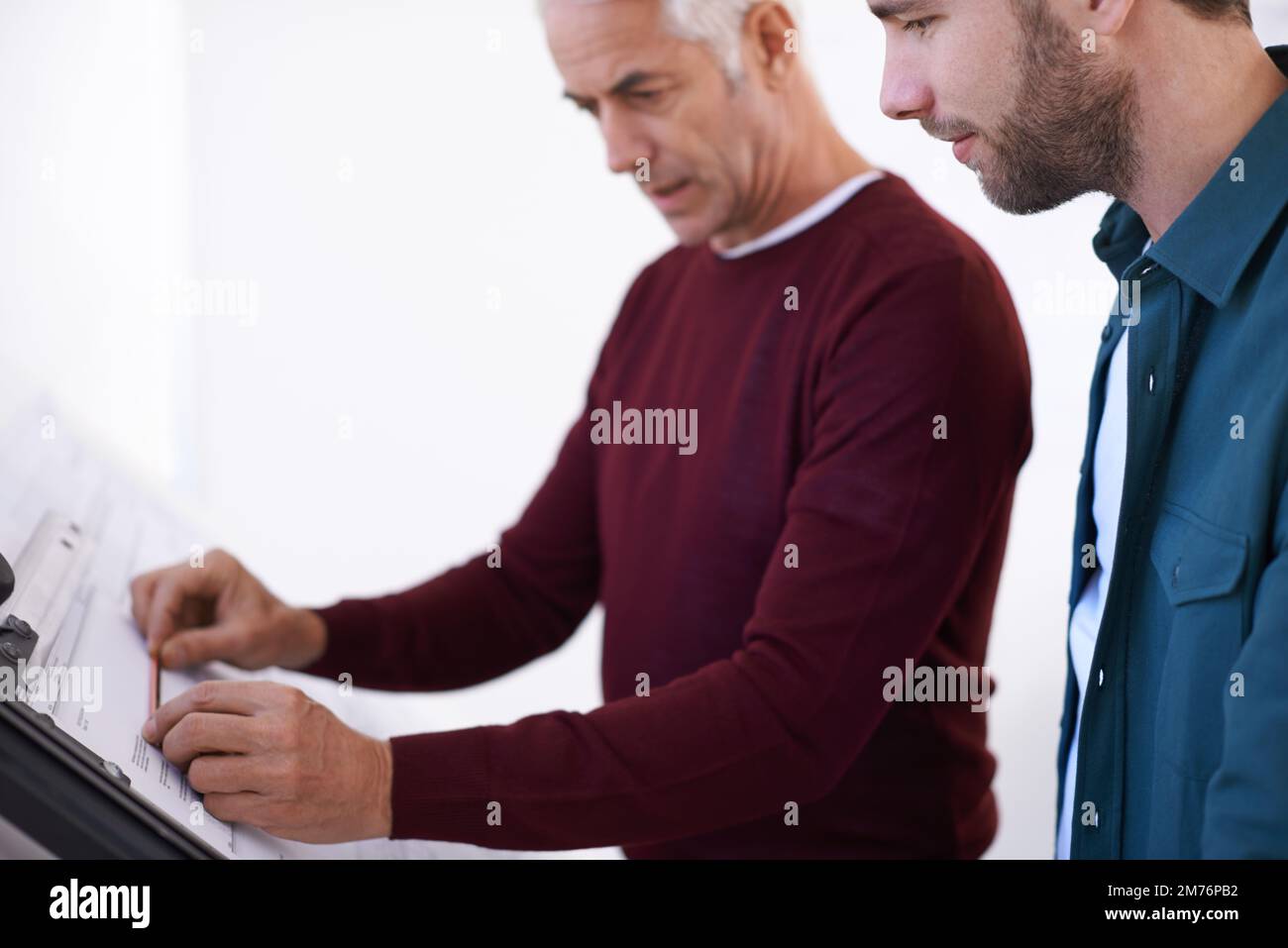 Some advice from an experienced colleague. two male architects working on a building plan at a drawing board. Stock Photo