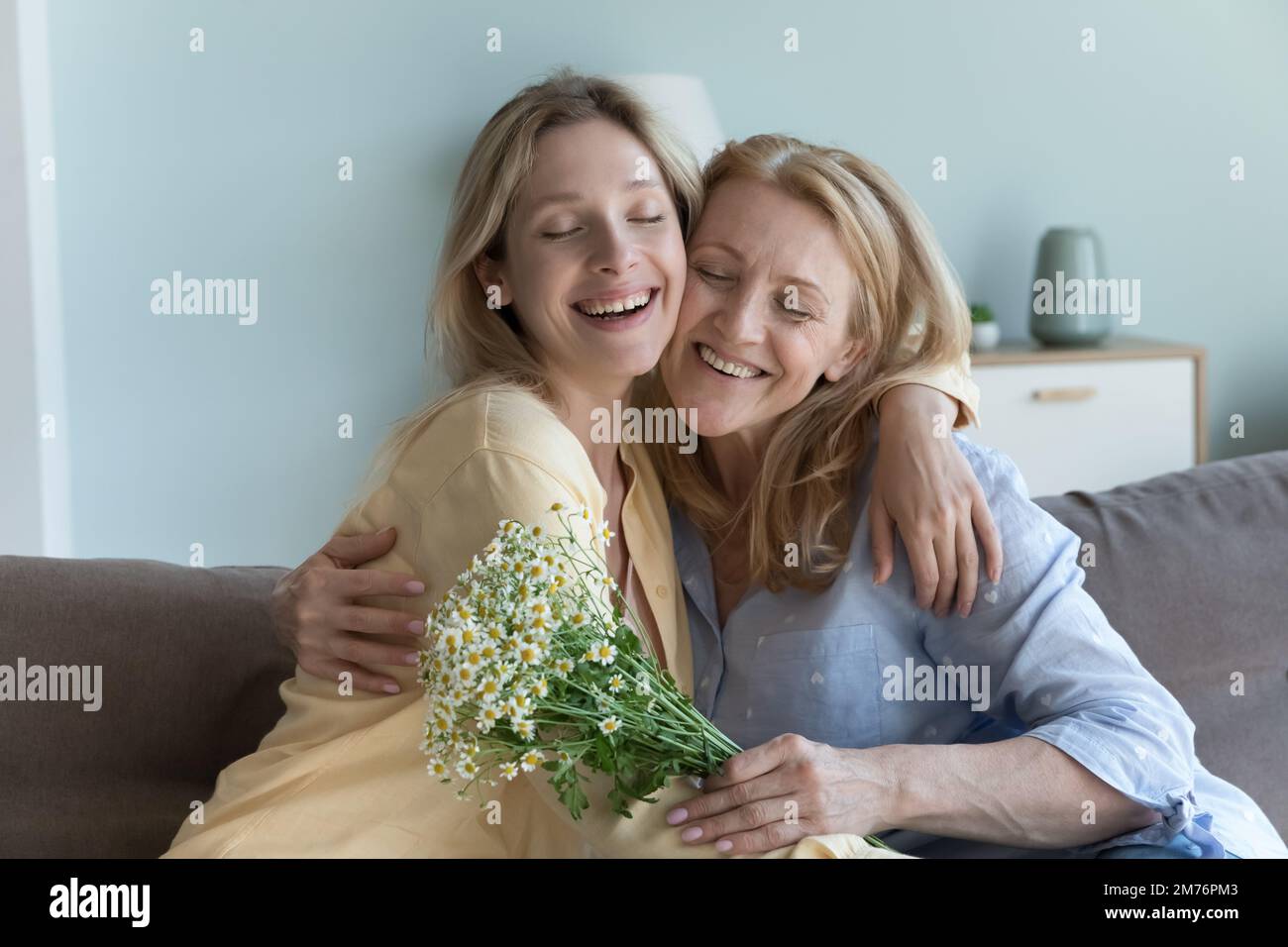 Happy peaceful young adult daughter girl giving flowers to mom, Stock Photo