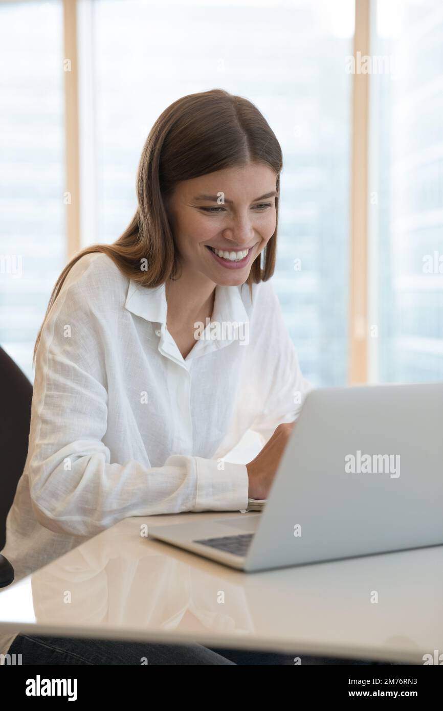 Woman sits at desk work online on laptop, vertical view Stock Photo