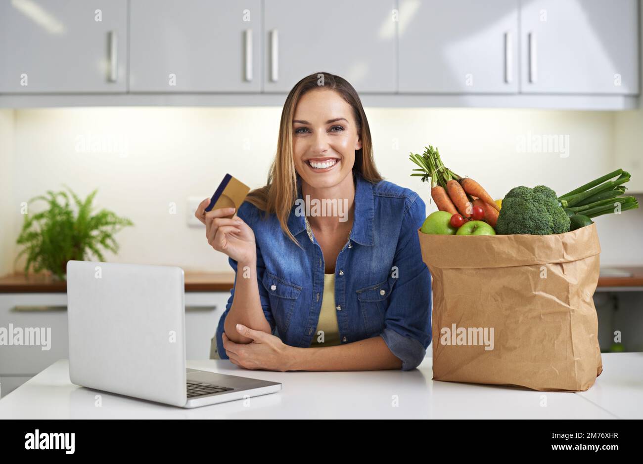 Making shopping a breeze. a young woman doing some online shopping with her groceries beside her. Stock Photo