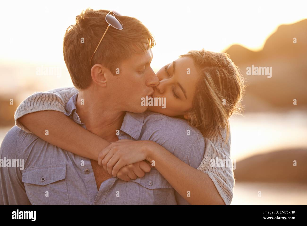 When Im with you the only place I want to be is closer. a happy young couple enjoying a piggyback ride and a kiss on the beach at sunset. Stock Photo