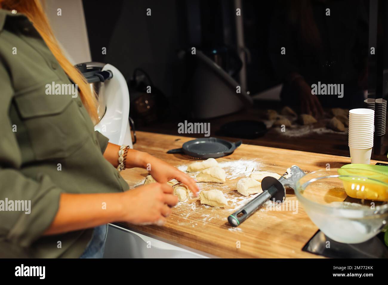 Hands of woman holding formed piece of raw dough. Cutting dough into pieces with knife. Cooking at home kitchen. Stock Photo