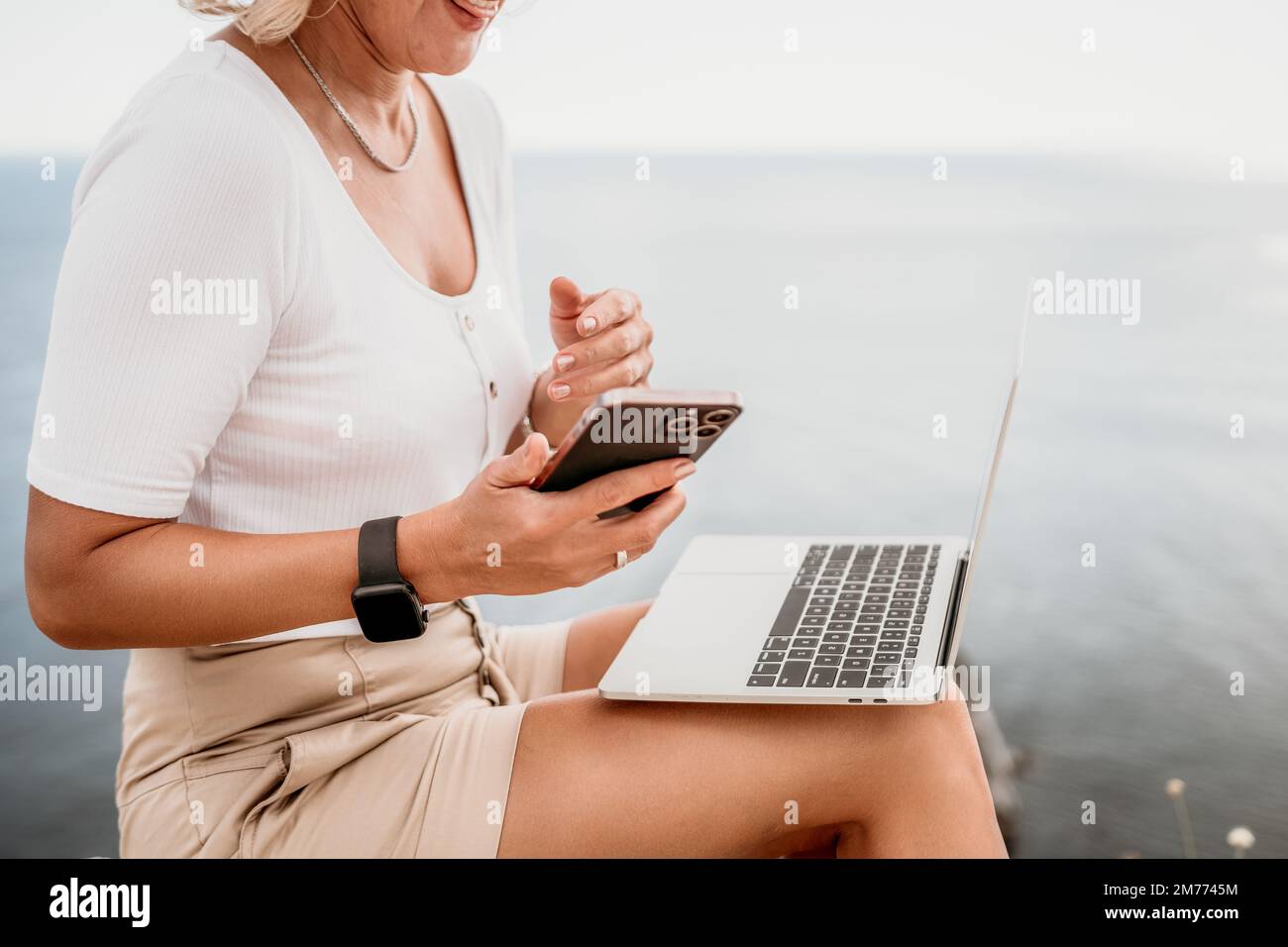 Digital nomad, Business woman working on laptop by the sea. Pretty lady typing on computer by the sea at sunset, makes a business transaction online Stock Photo