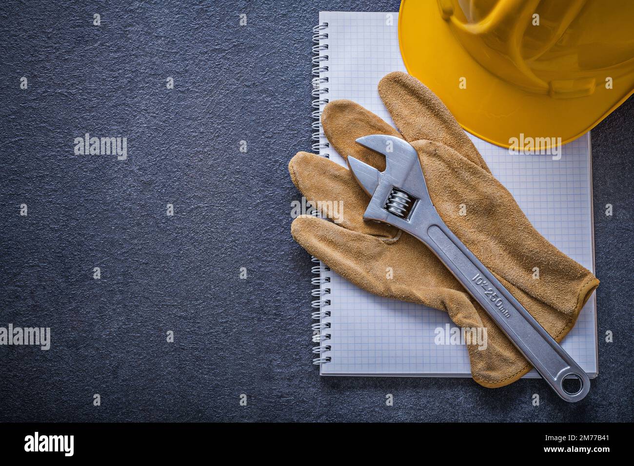 Notebook hard hat adjustable wrench protective gloves construction concept. Stock Photo