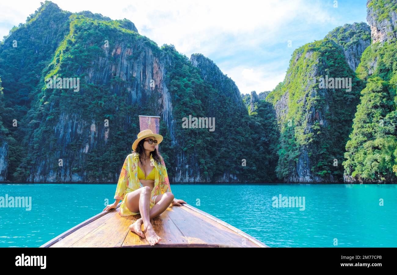 Asian women in front of a longtail boat at Kho Phi Phi Thailand, women in front of a boat at Pileh Lagoon with turqouse colored ocean Stock Photo