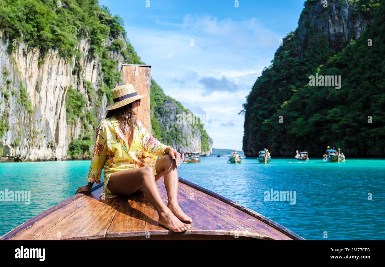 Asian women in front of a longtail boat at Kho Phi Phi Thailand, women in front of a boat at Pileh Lagoon with turqouse colored ocean Stock Photo