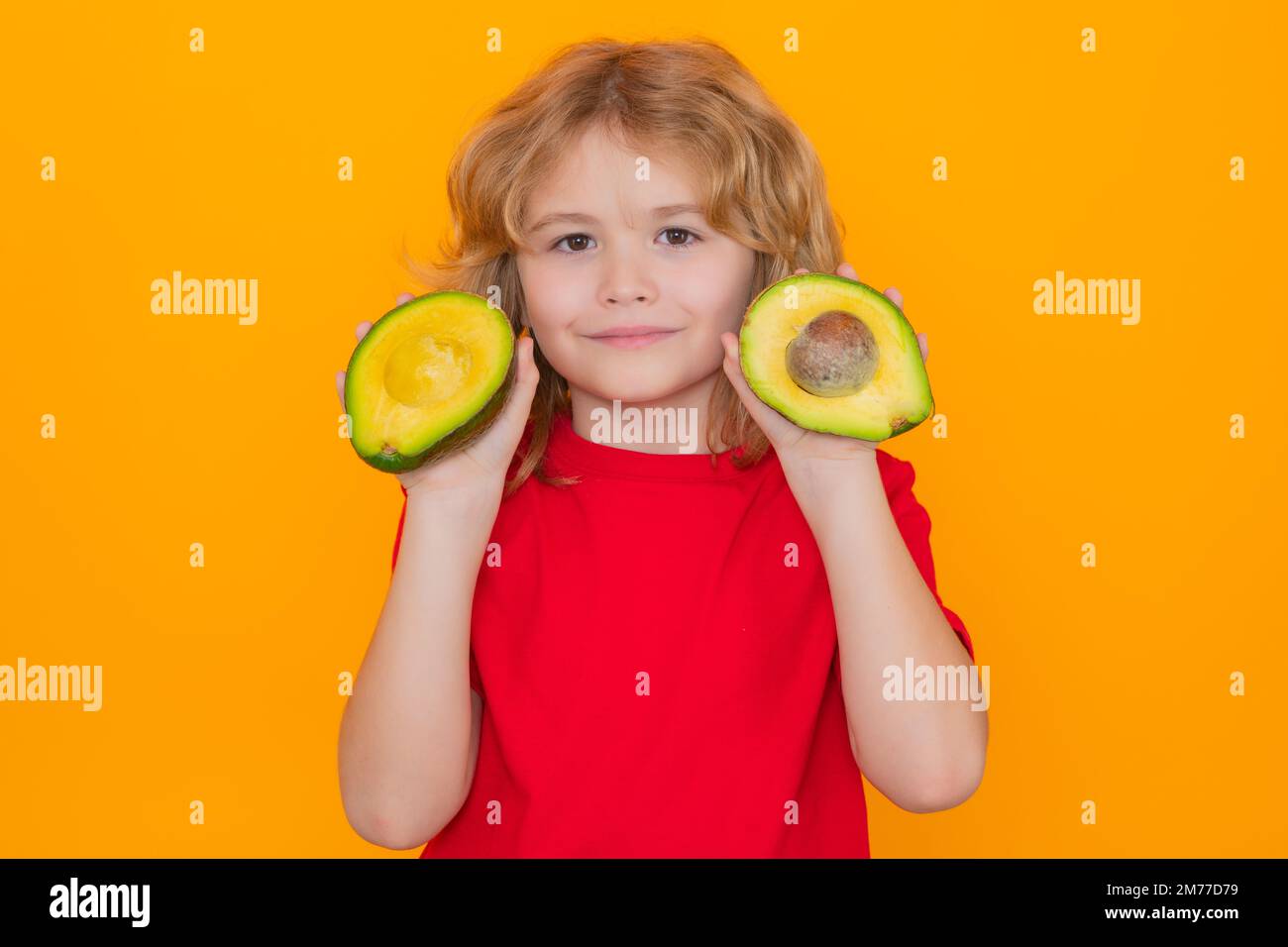 Healthy fruits and vegetables for kids. Kid hold red avocado in studio. Studio portrait of cute child with avocado isolated on yellow background. Stock Photo