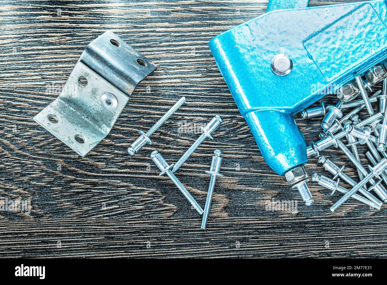 Riveting pliers rivets steel screws on wooden board. Stock Photo