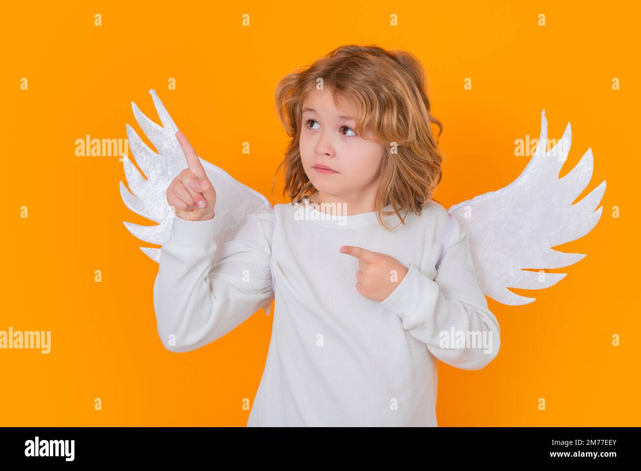 Child angel pointing finger, point gesture. Valentines day banner. Cute child with angel wings. Studio portrait of angel child on studio color Stock Photo