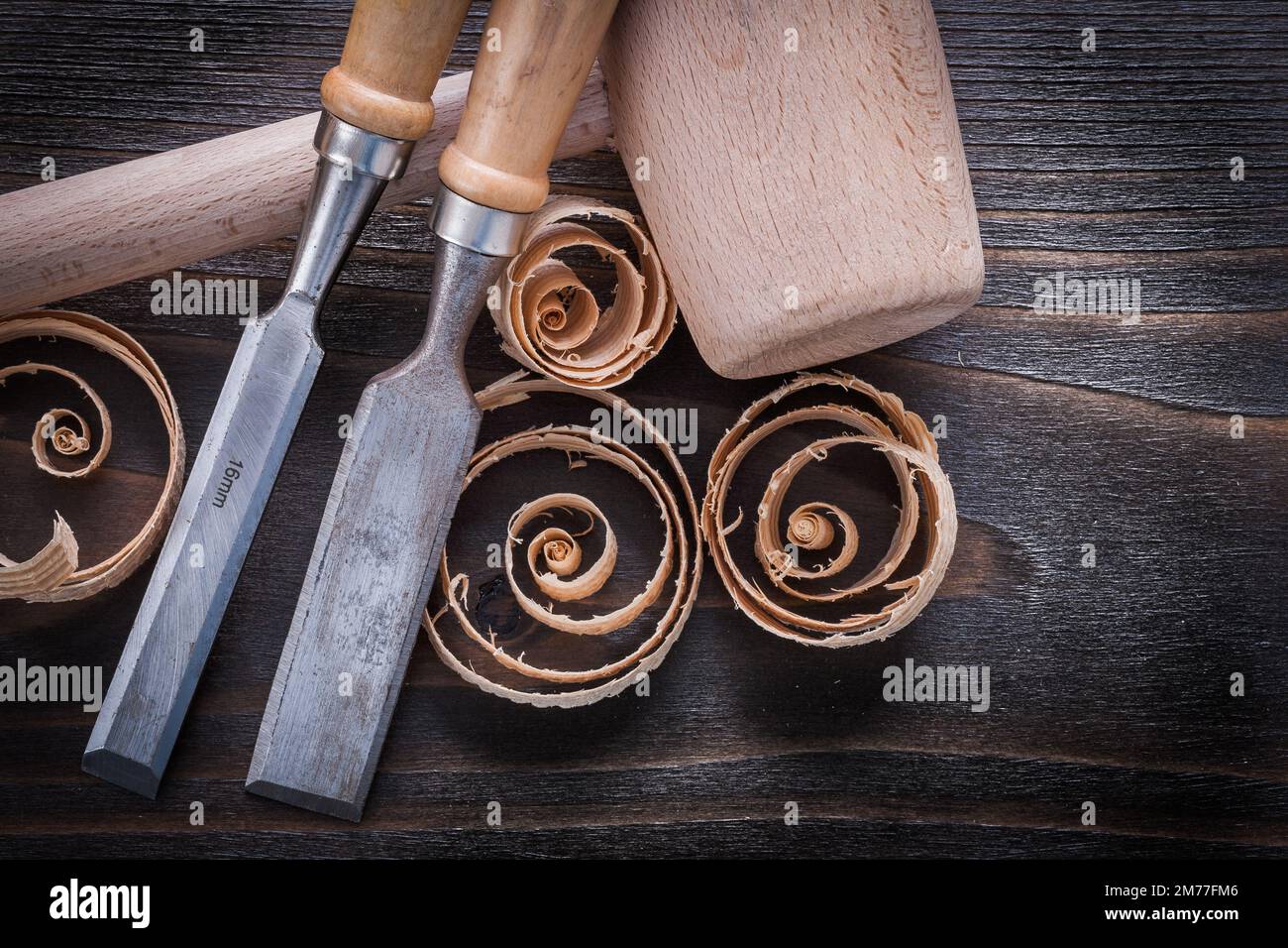 Set of wooden hammer firmer chisels and curled up shavings on vintage wood board construction concept. Stock Photo