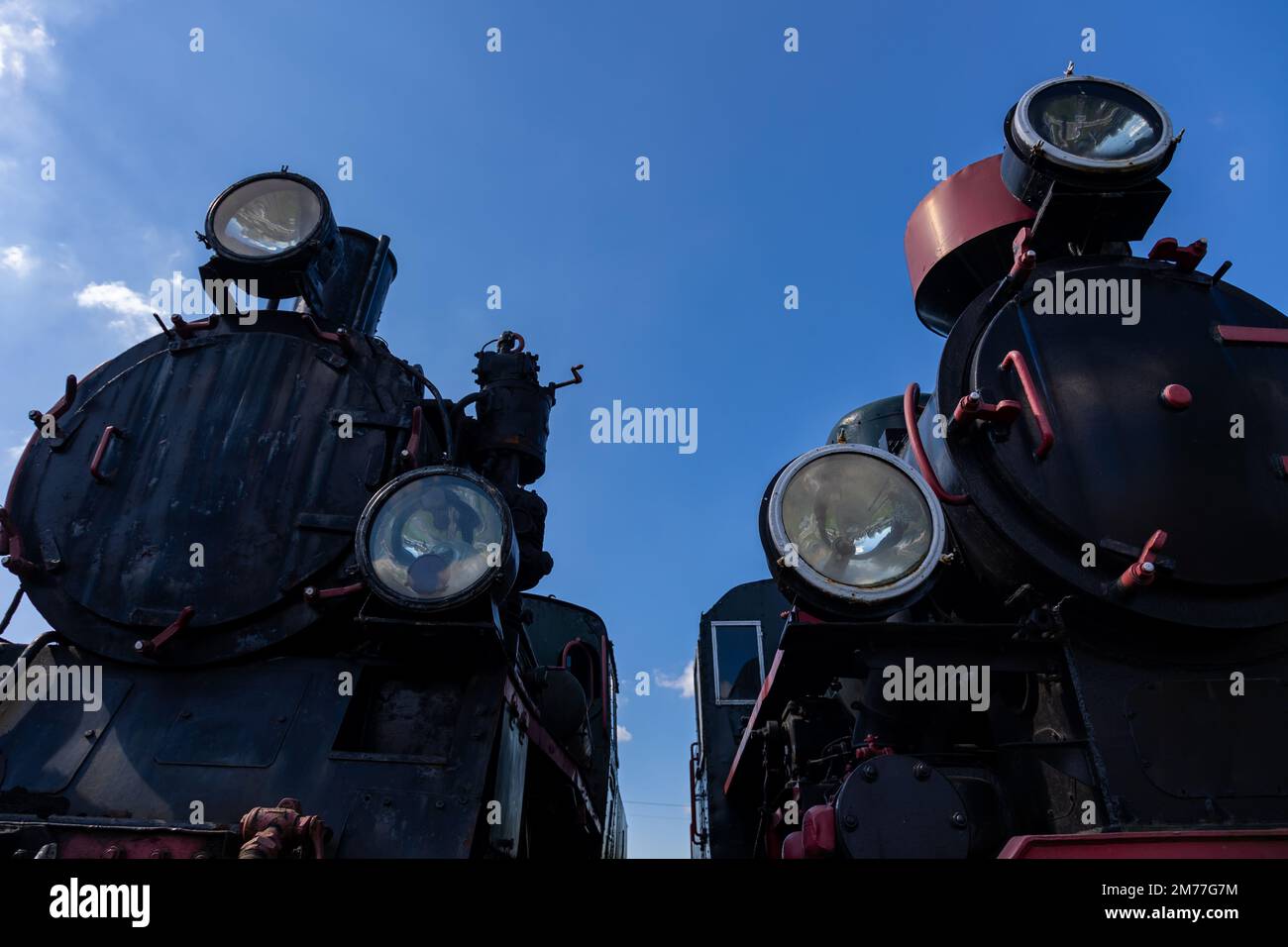 Front view of two steam locomotives standing side by side. Bottom view showing objects against a blue sky Stock Photo
