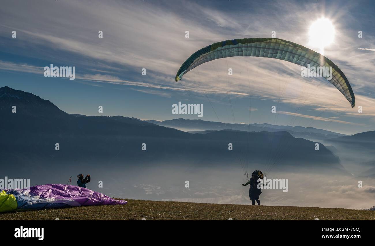 Men on a grassy slope prepare the glider for paragliding from Vetriolo Terme, Trento province - Trentino Alto Adige - Paragliding school - Italy Stock Photo