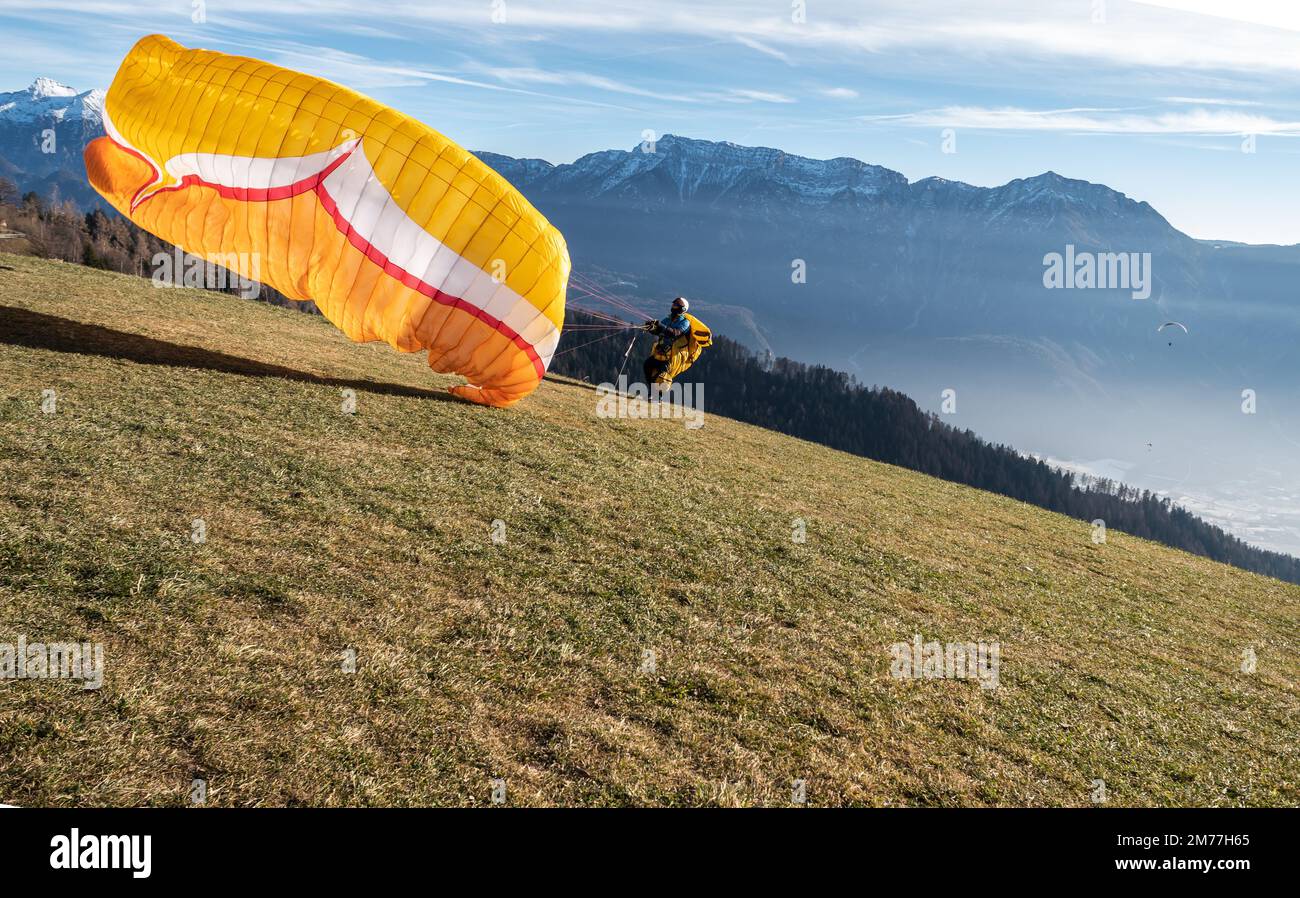 Man on a grassy slope prepare the glider for paragliding from Vetriolo Terme, Trento province - Trentino Alto Adige - Paragliding school - Italy Stock Photo