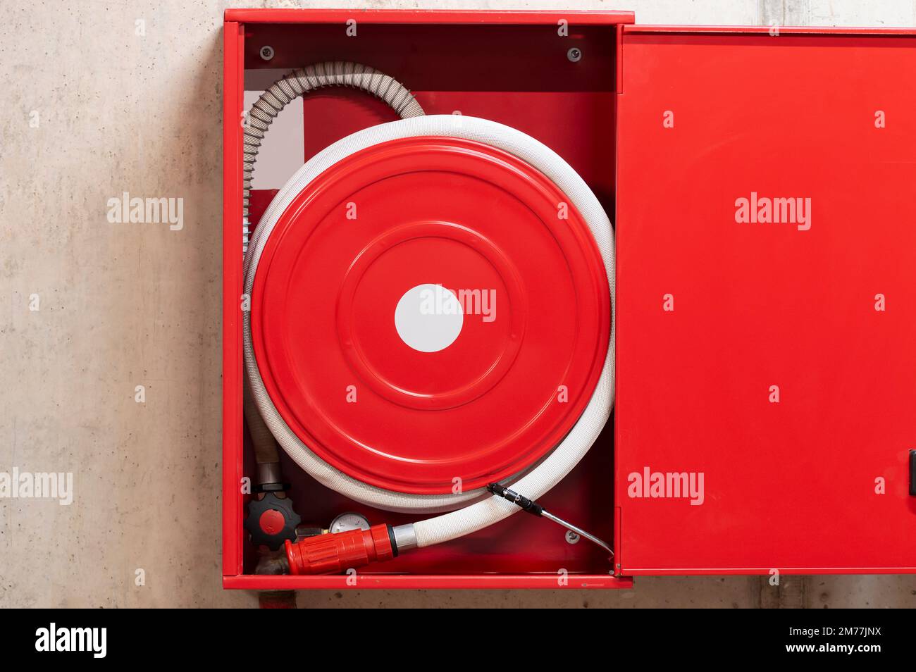 Red fire hose reel, mounted on a concrete wall background. Stock Photo