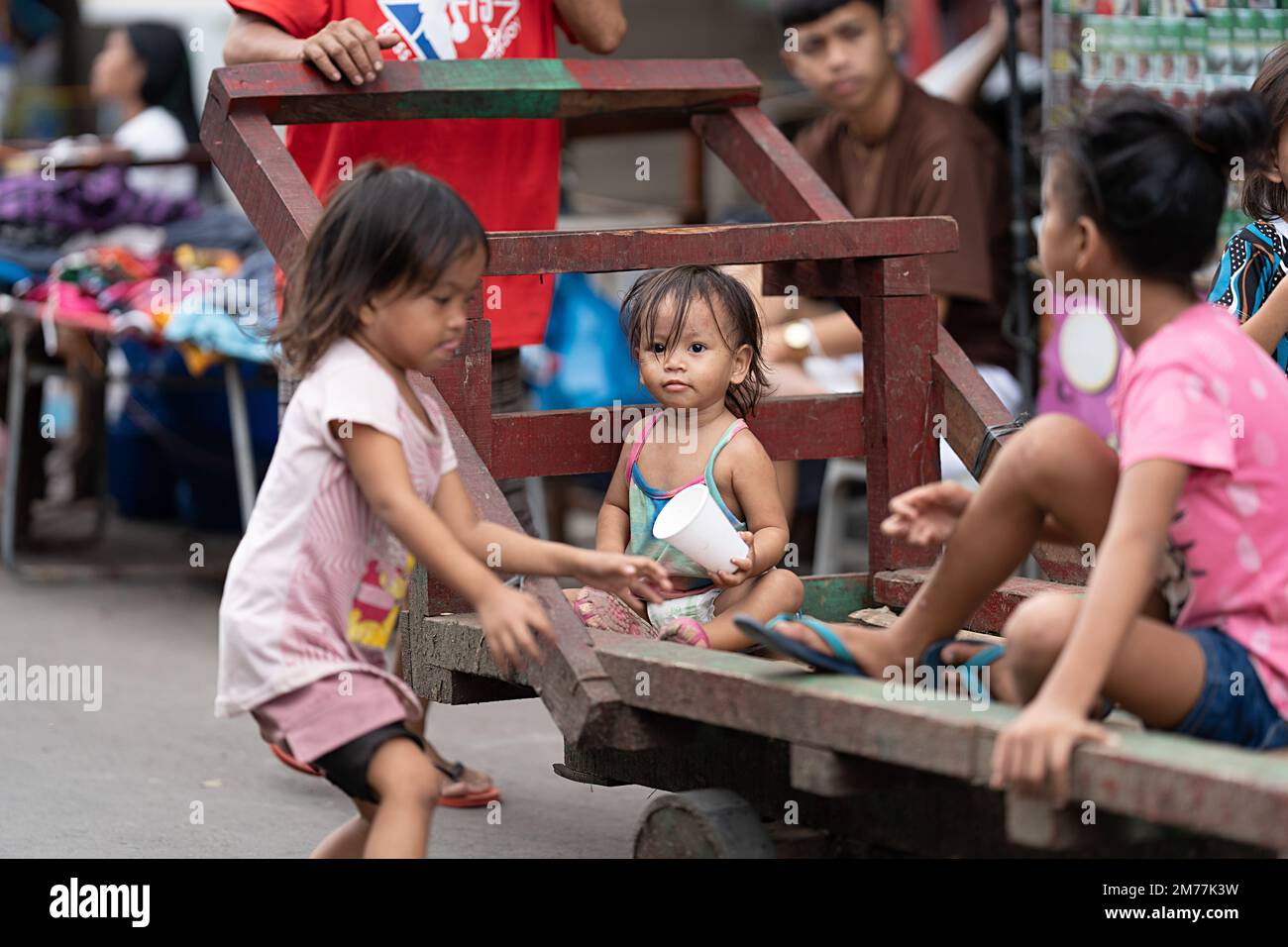 Young children in a poor community ride on a wooden pushcart, Philippines. Stock Photo