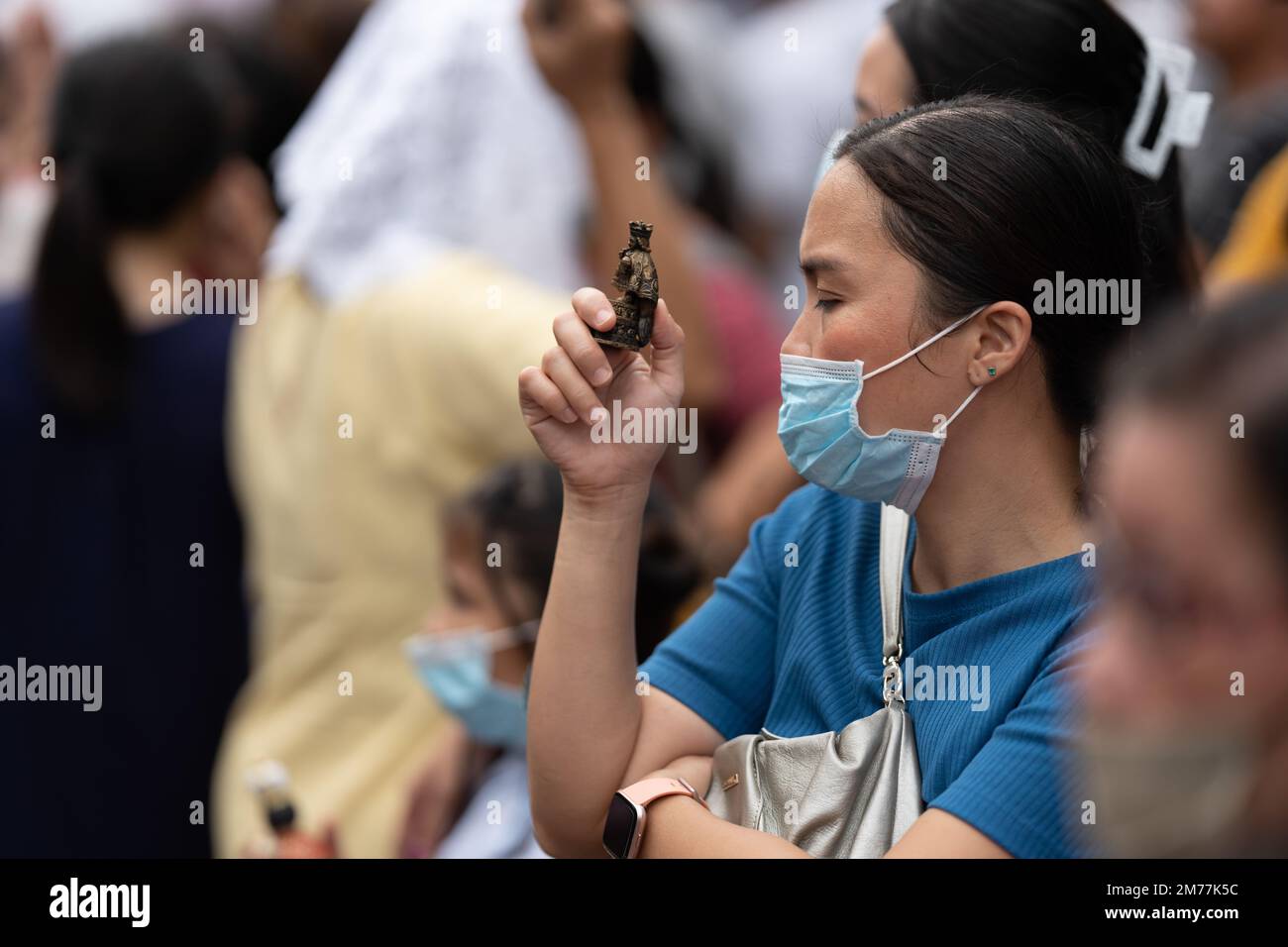 A Filipino Catholic holding a Santo Nino figurine whilst praying outside of the Basilca Church in CEbu City, Philippines Stock Photo