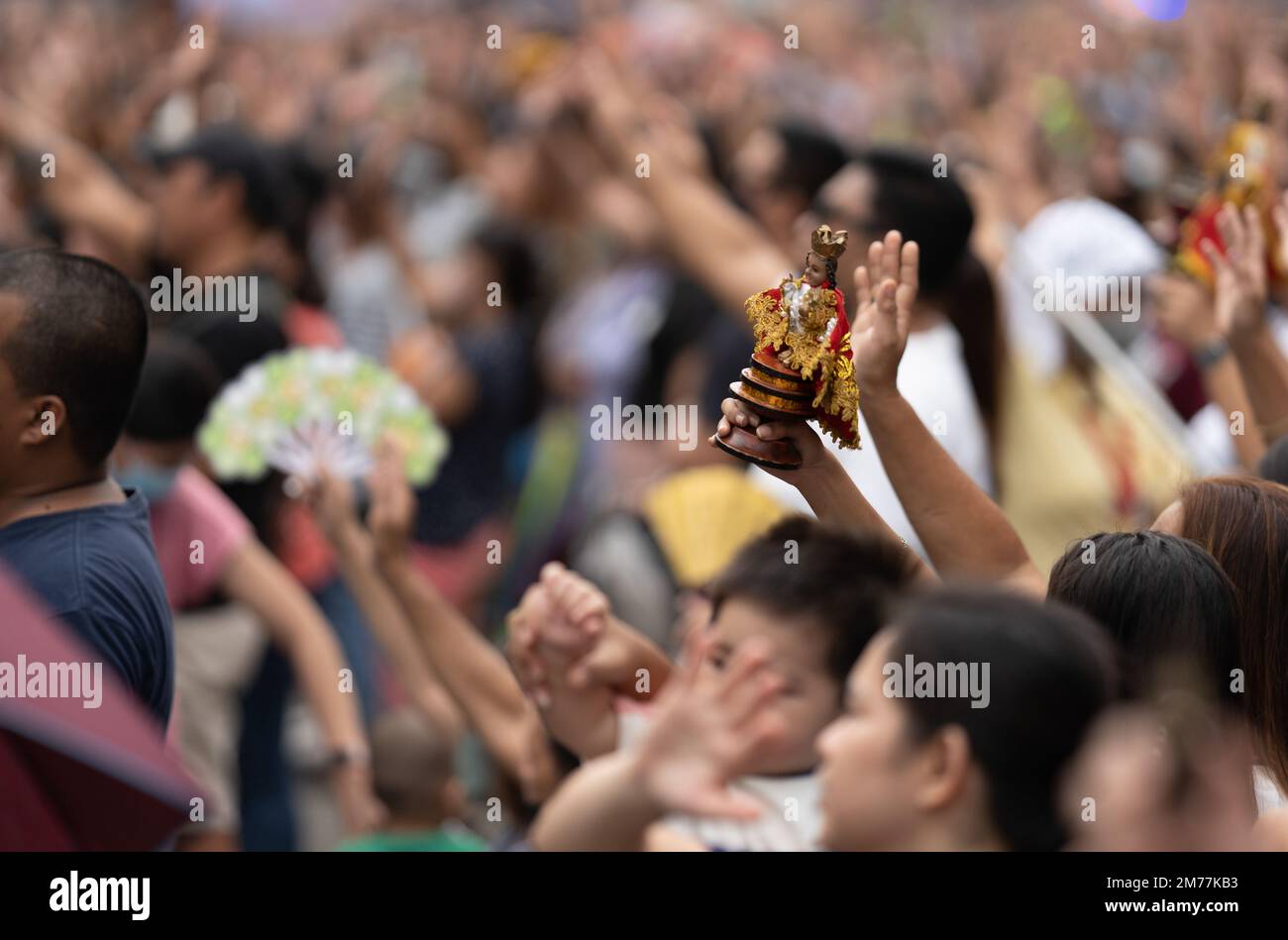 Filipino Catholics wave their hands in the air and hold up Santo Nino figurines whilst the religious song Batobalani sa Gugma is being played at the B Stock Photo