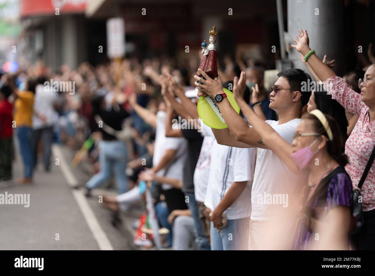 Filipino Catholics wave their hands in the air and hold up Santo Nino figurines whilst the religious song Batobalani sa Gugma is being played at the B Stock Photo