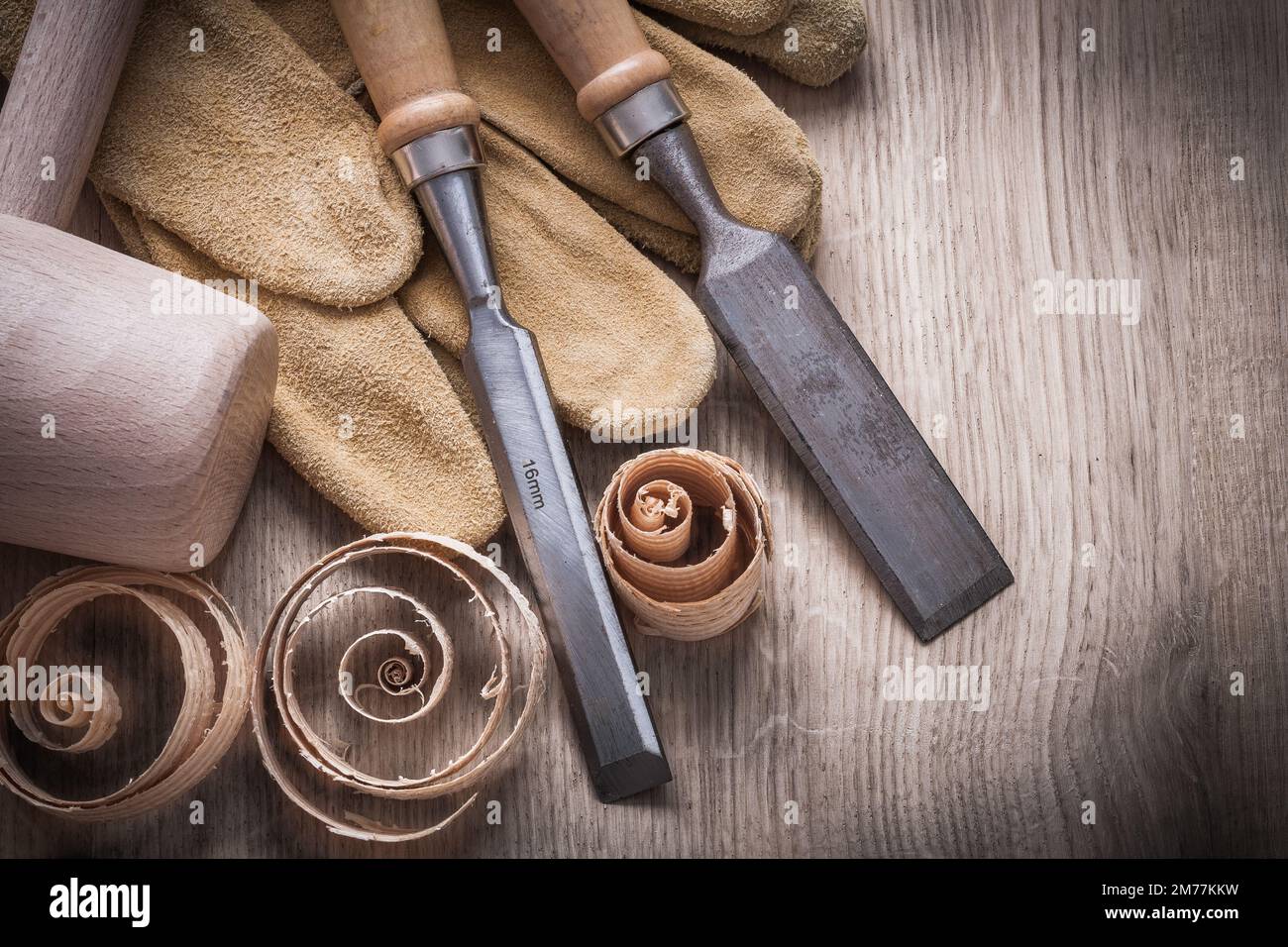 Wooden mallet curled up planning chips firmer chisels leather gloves on wood board construction concept. Stock Photo